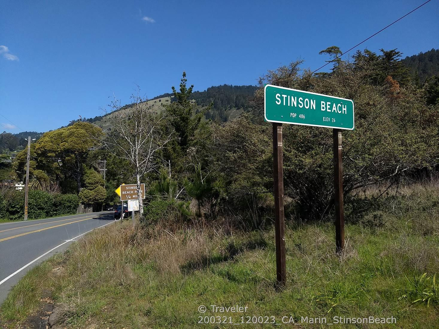 Roadside sign next to a paved road, with green hills and trees.