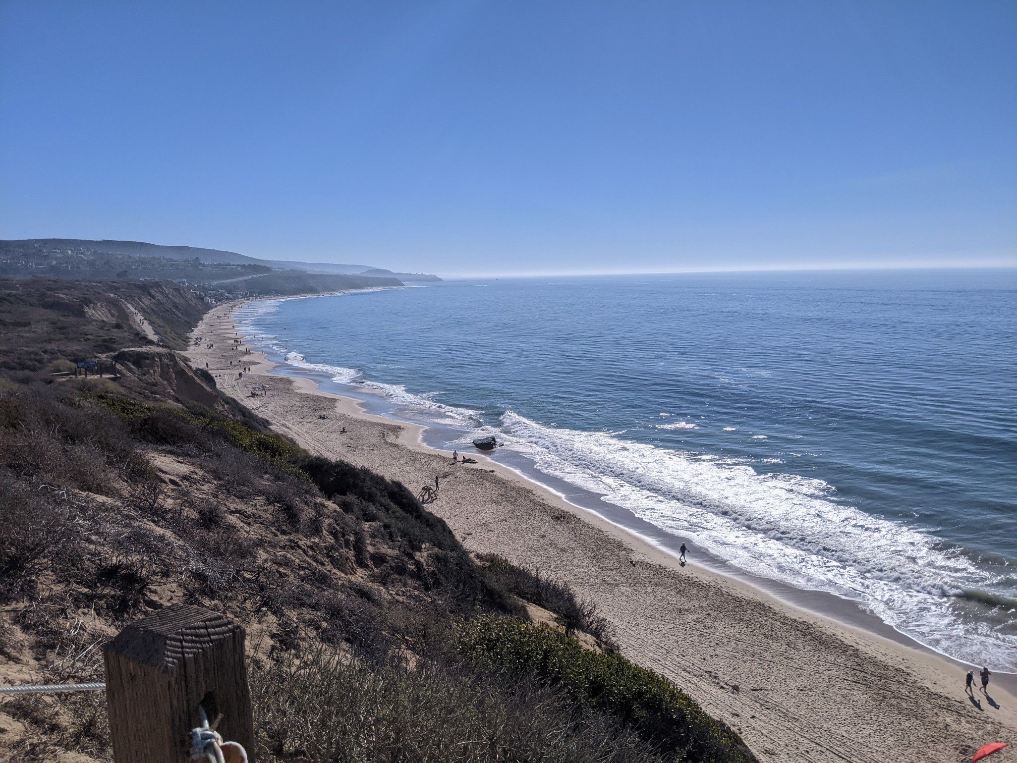 Bright coastal view of a wide sandy beach, blue ocean, and dry cliffs. - Crystal Cove Trail