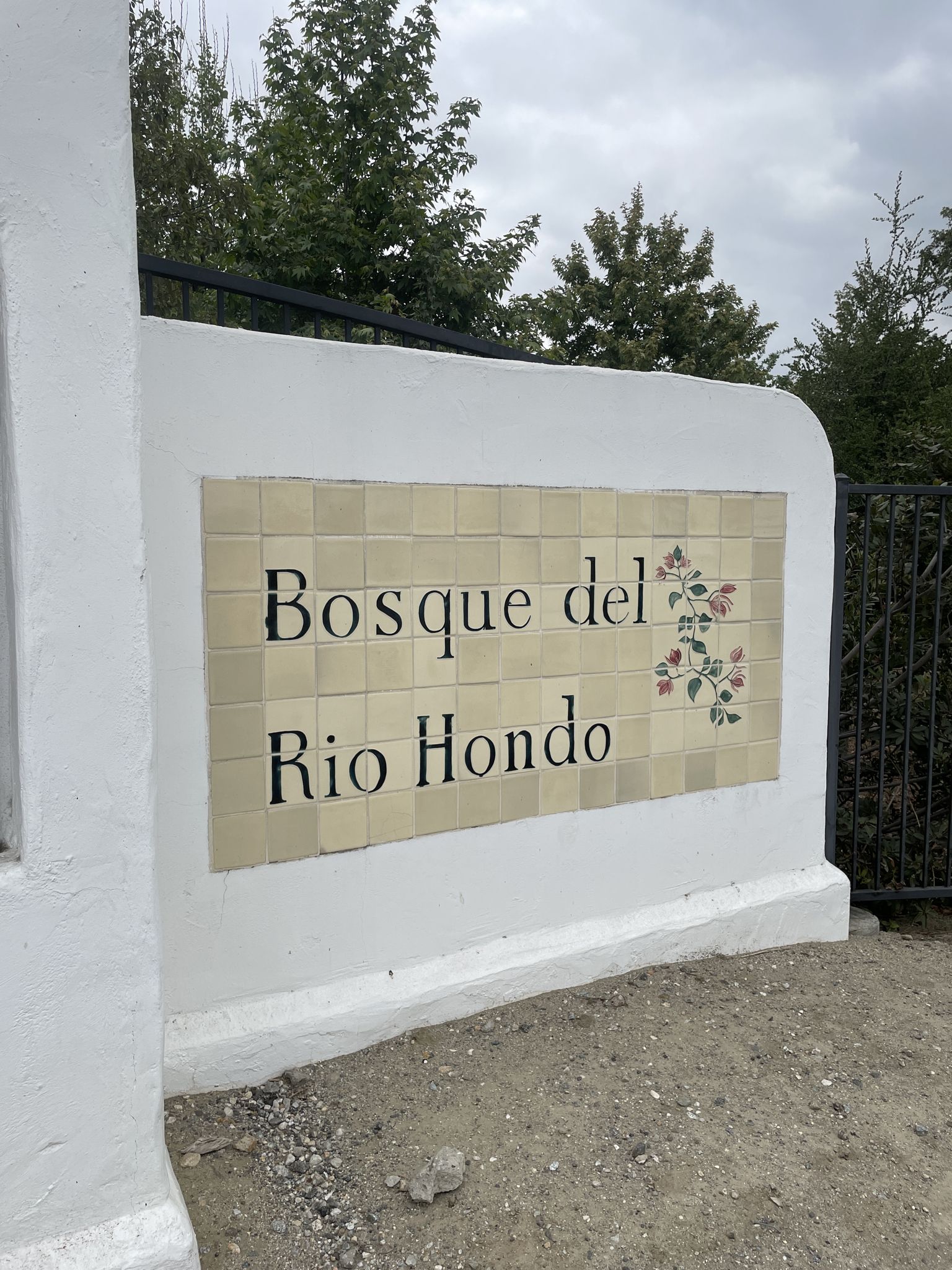 Tiled sign on a white wall with green trees in background. - Rio Hondo River Trail