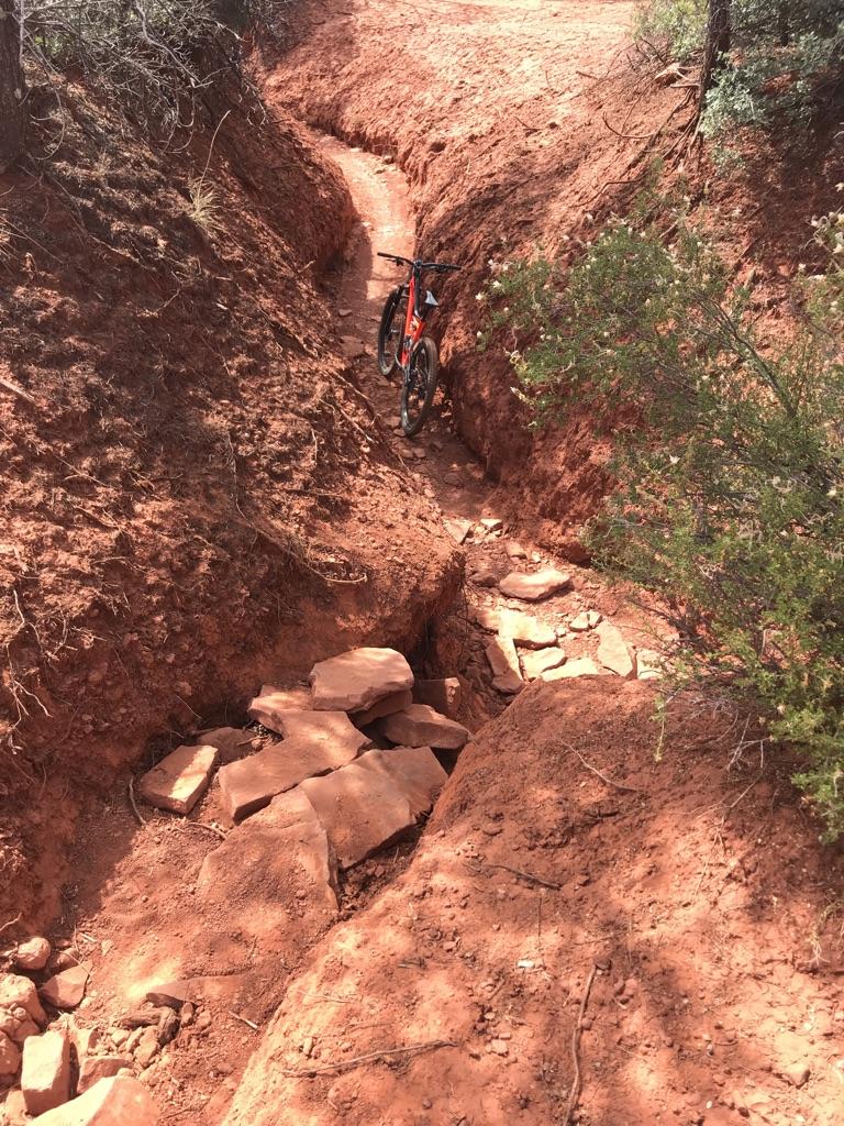 A mountain bike rests in a deep, narrow red dirt gully.
