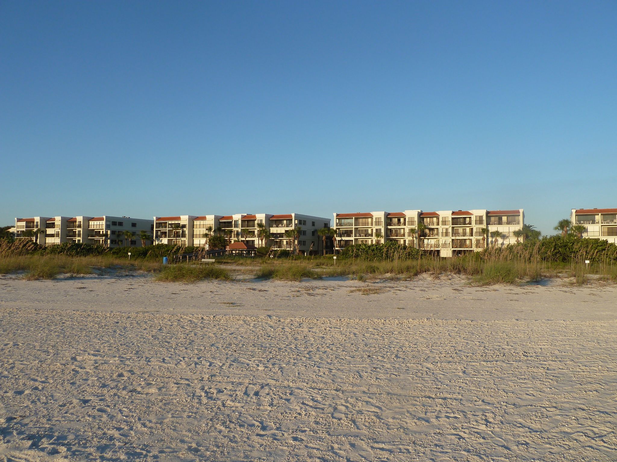 Row of buildings visible across a wide, sunny, sandy beach. - Sunset Beach Scenic Boardwalk Loop