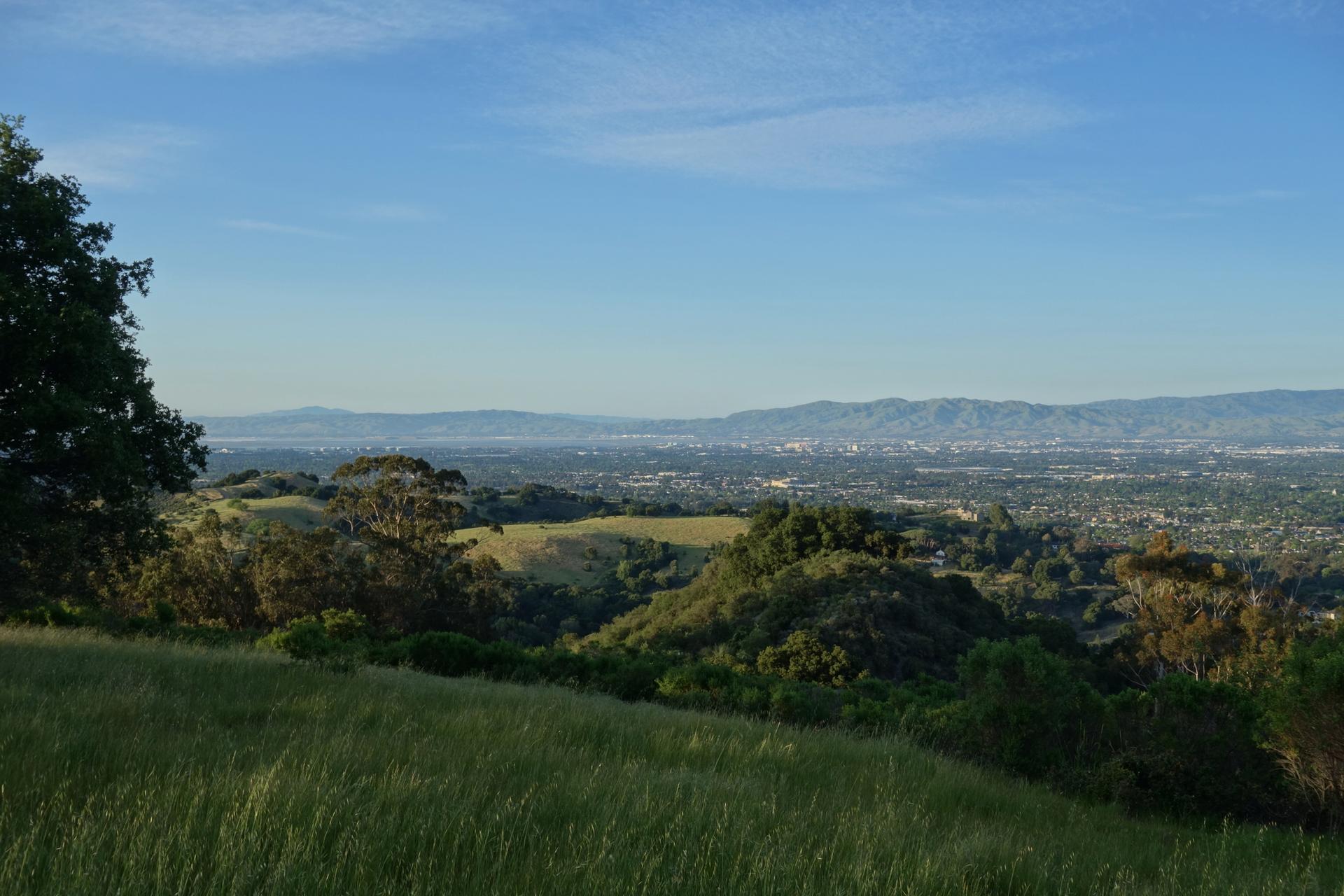Panoramic view from a grassy hillside overlooking a distant city and mountains.