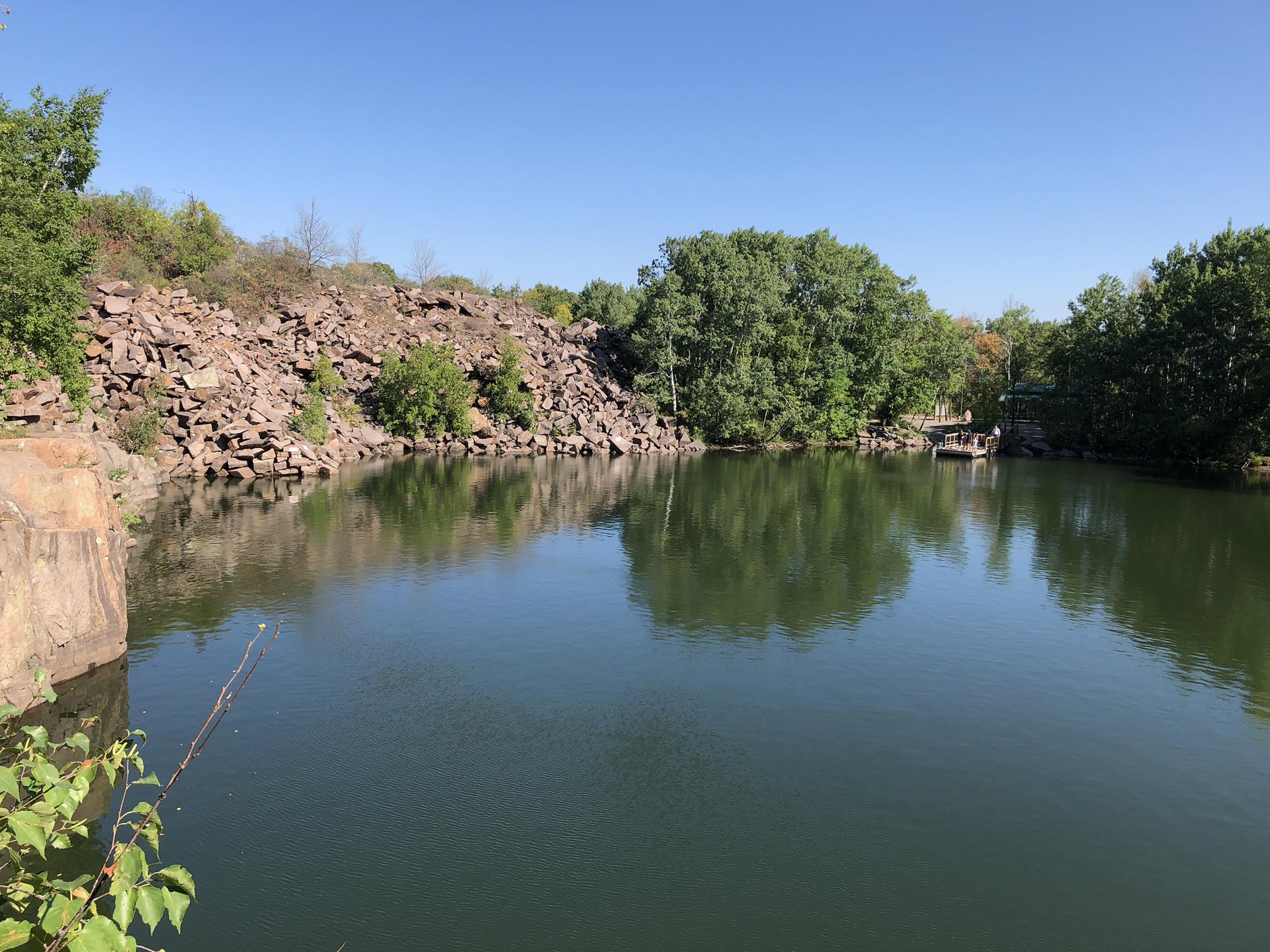 Calm lake surrounded by rocky banks and green trees under a blue sky.