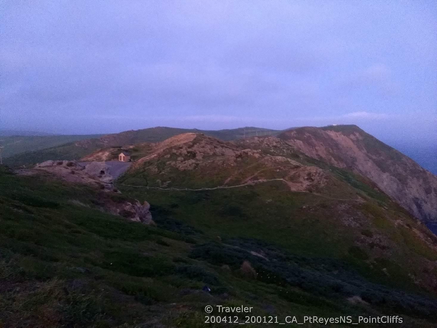 Small building on green rolling hillsides under a twilight sky.