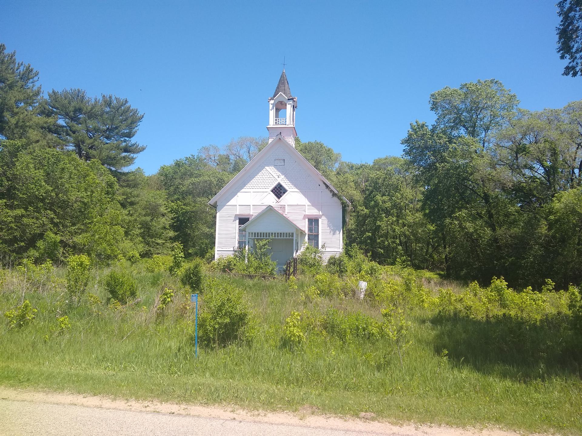 A small white church with a steeple, surrounded by green trees and grass.