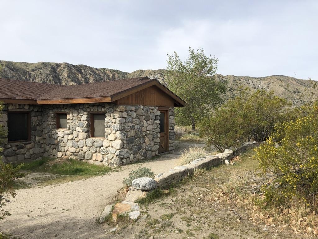 Stone cabin with a brown roof in a dry, hilly landscape.