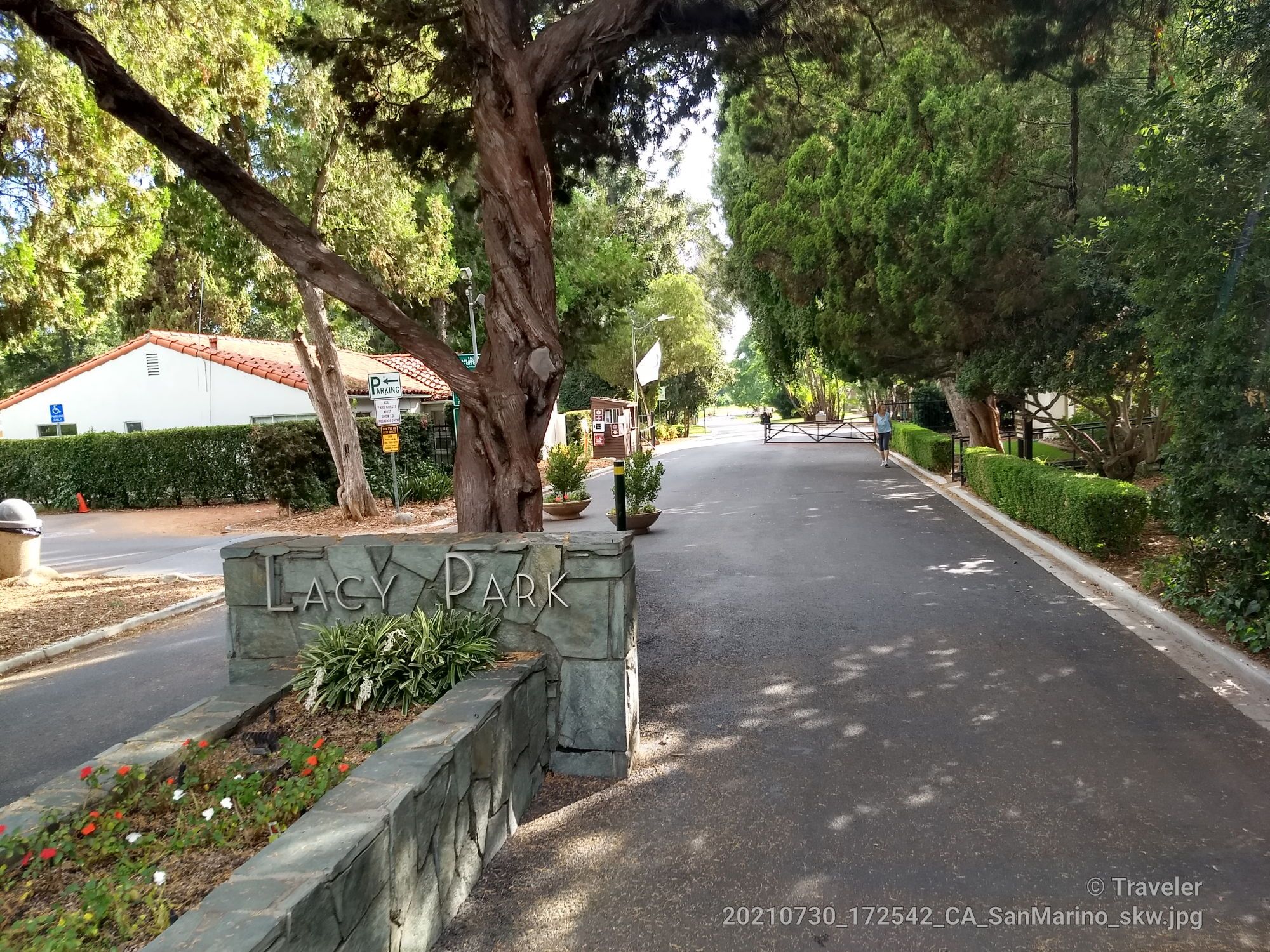 A stone park sign next to a paved road with trees and a distant person. - Lacy Park Loop