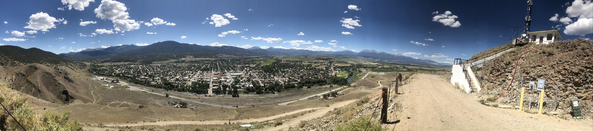 Panoramic view of a town in a valley, surrounded by mountains under a bright sky.
