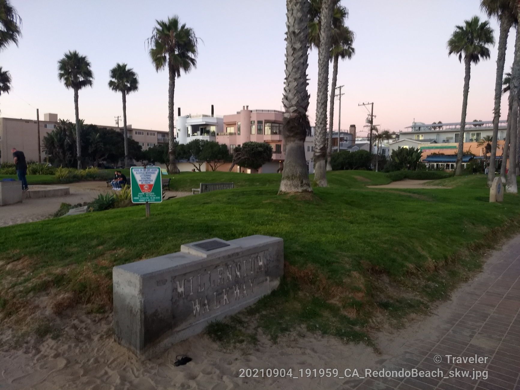 Grassy park with palm trees, stone bench, and distant buildings at dusk. - Noble Park loop from Manhattan Beach