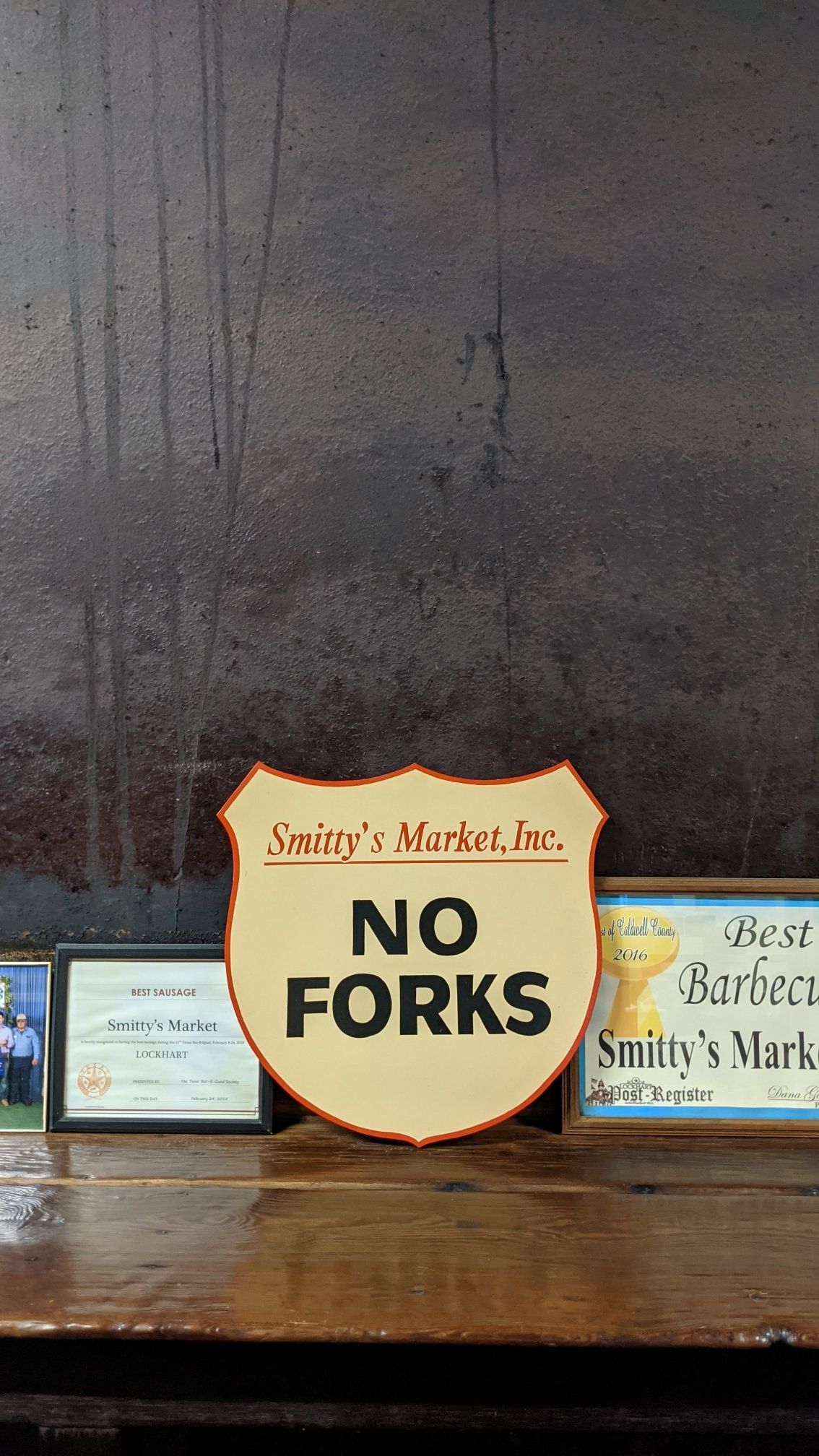 A "NO FORKS" sign on a wooden counter with awards in dim light. - San Marcos to Kyle & Lockhart for BBQ loop