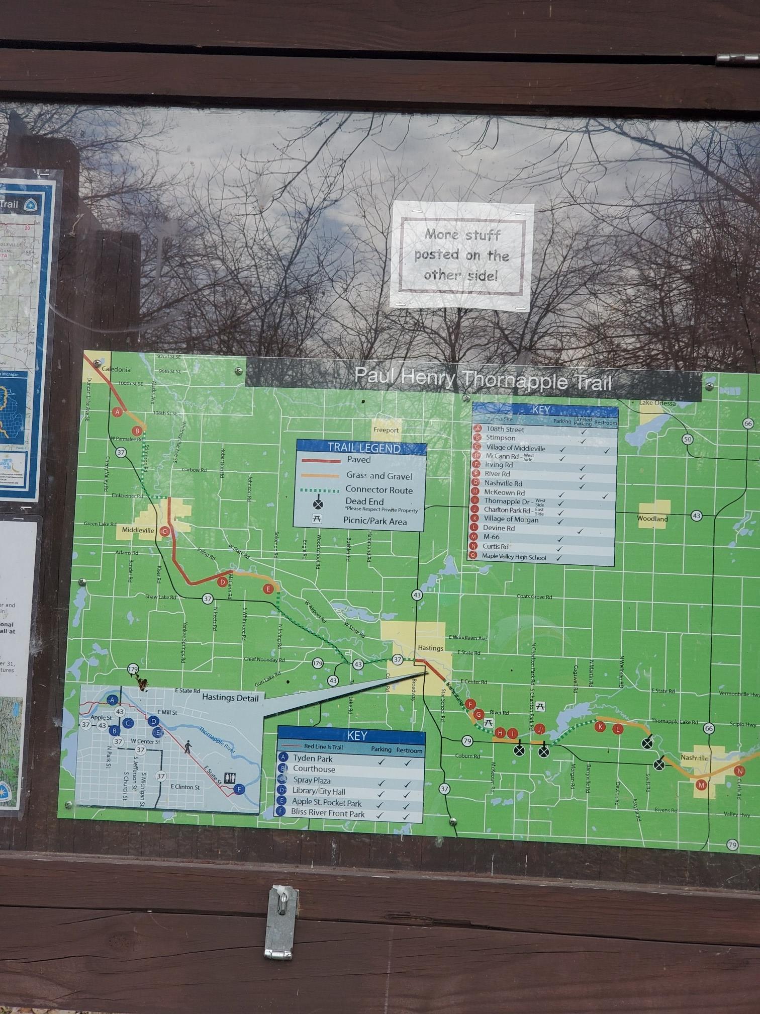 A trail map displayed behind glass on a wooden board, reflecting bare trees.