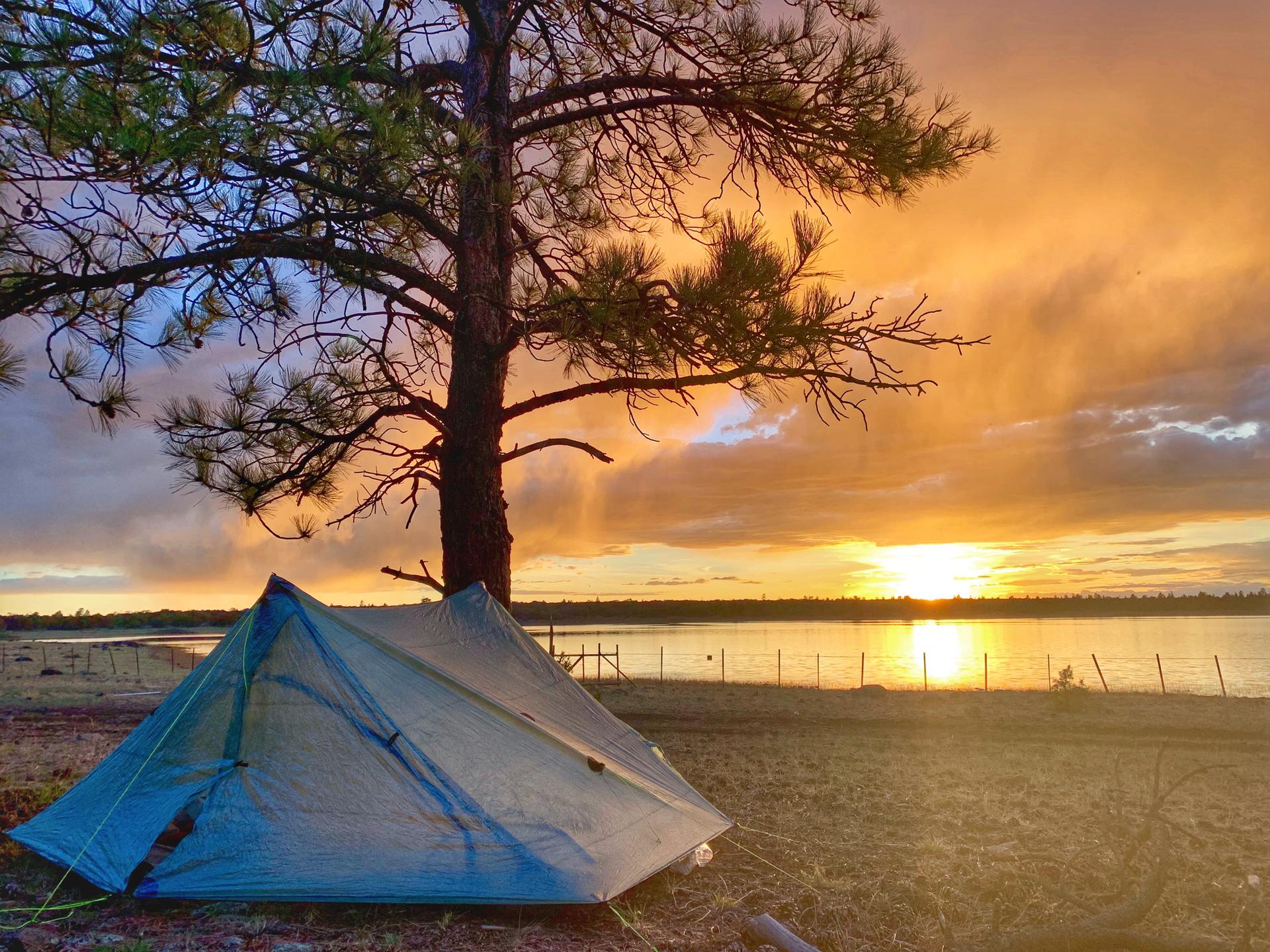 A light blue tent near a lake under a dramatic orange sunset.
