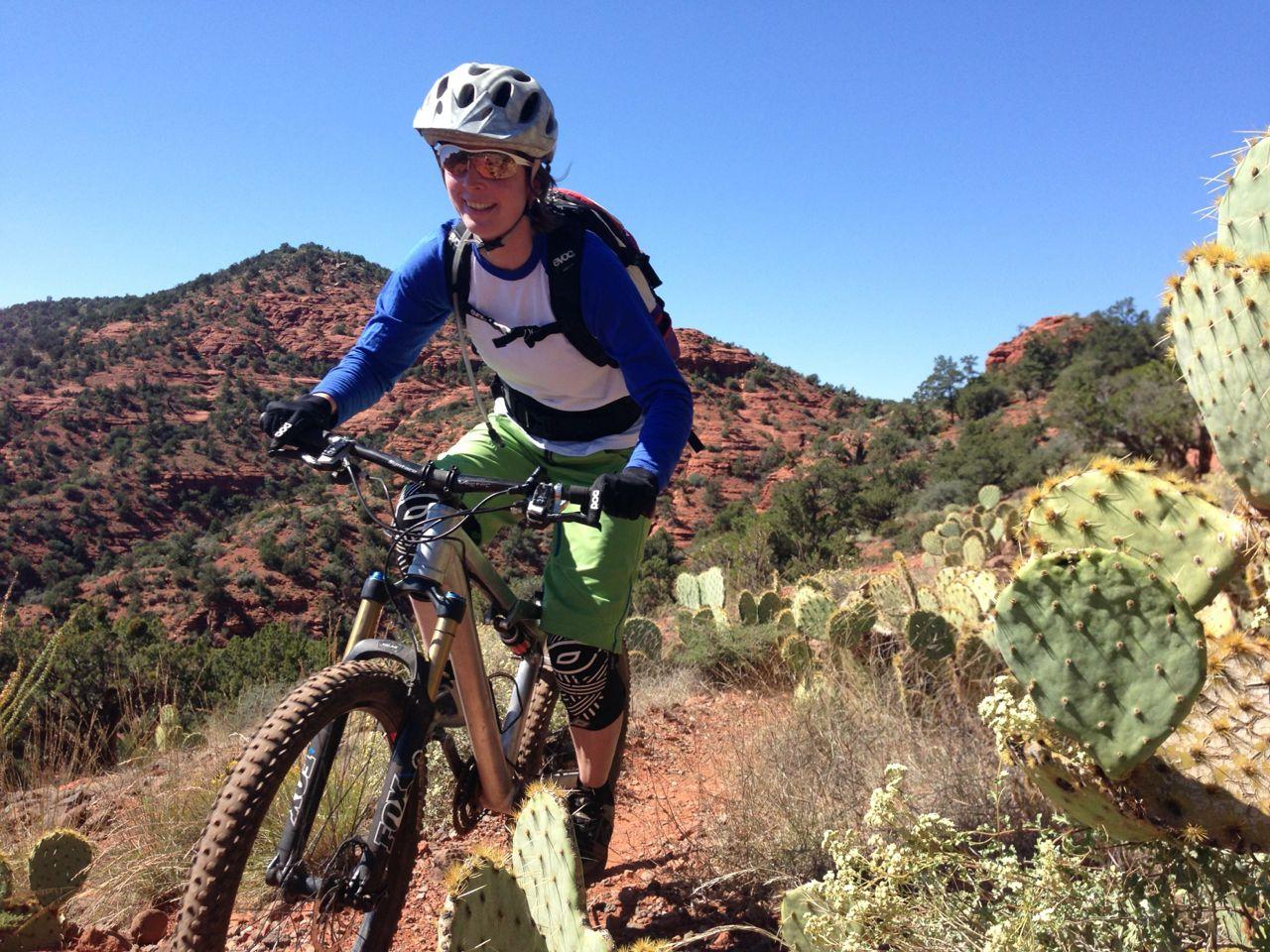 Mountain biker on a sunny desert trail with cacti and red rock hills.