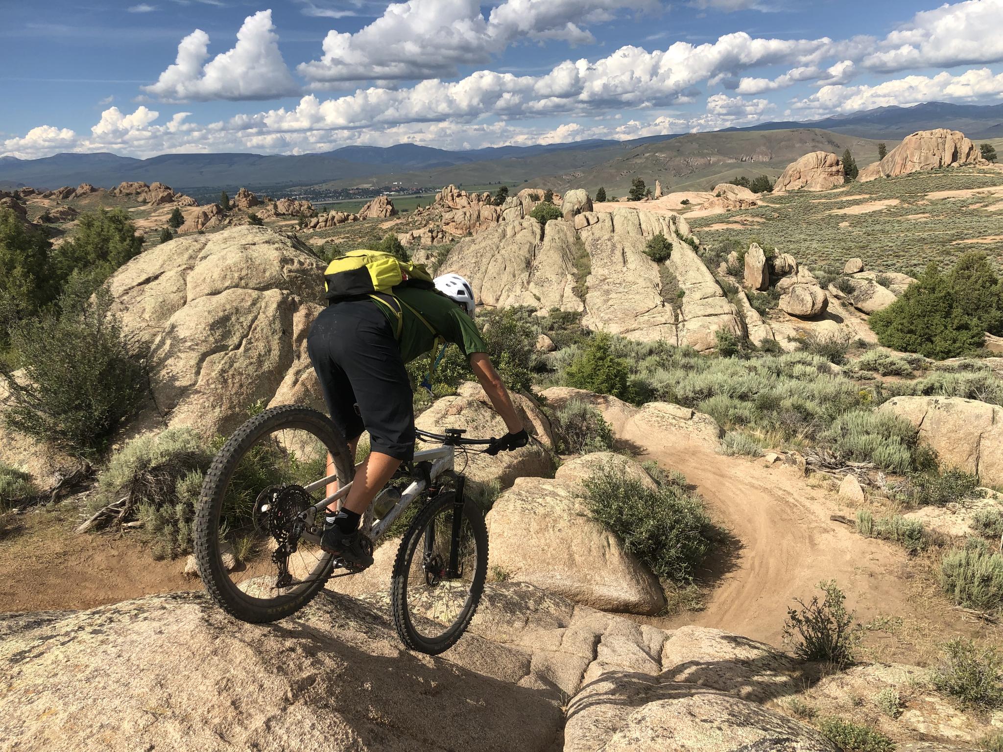 Mountain biker navigates a rocky, winding dirt trail on a sunny day.