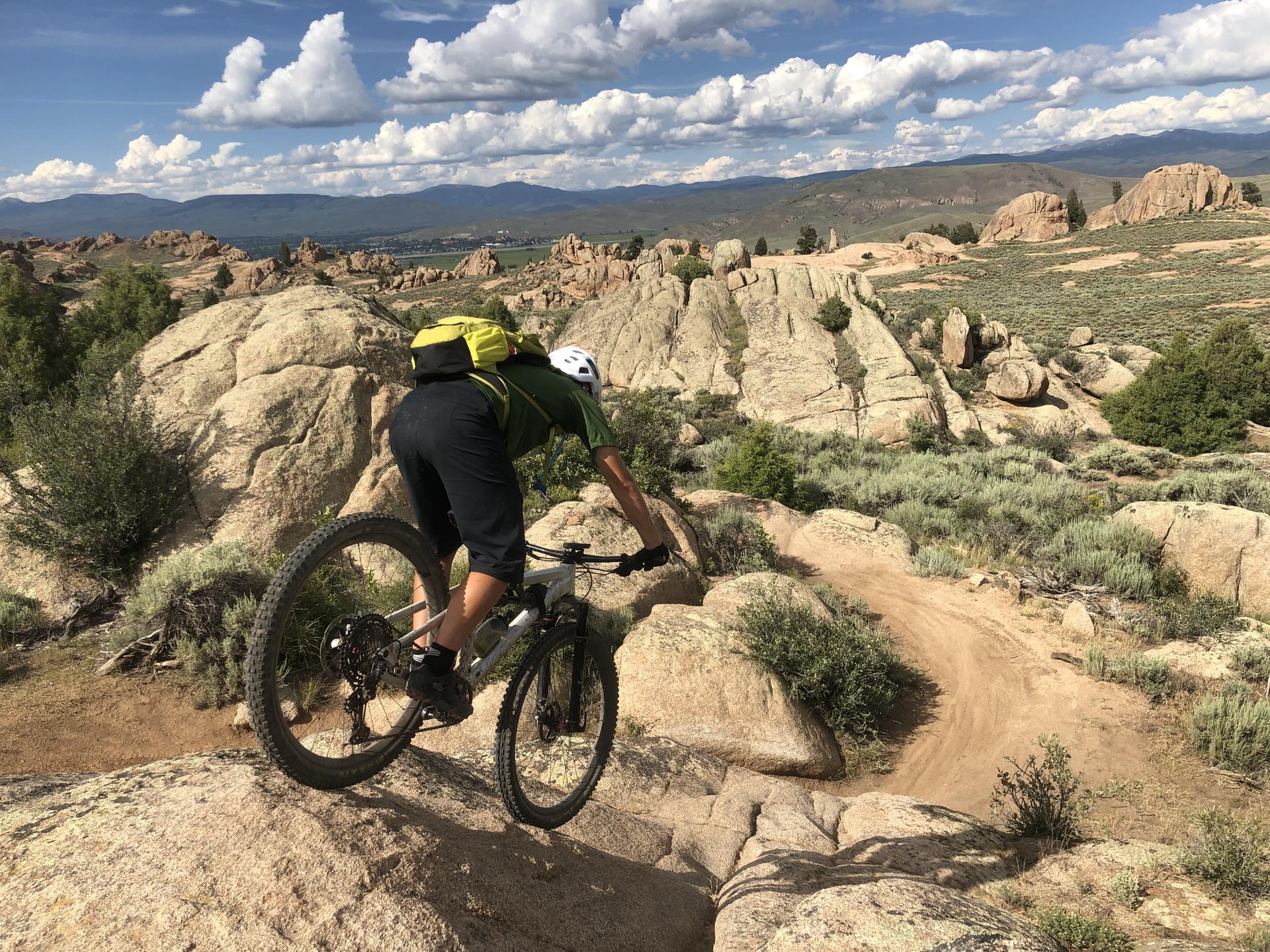 Mountain biker navigates a rocky, winding dirt trail on a sunny day.