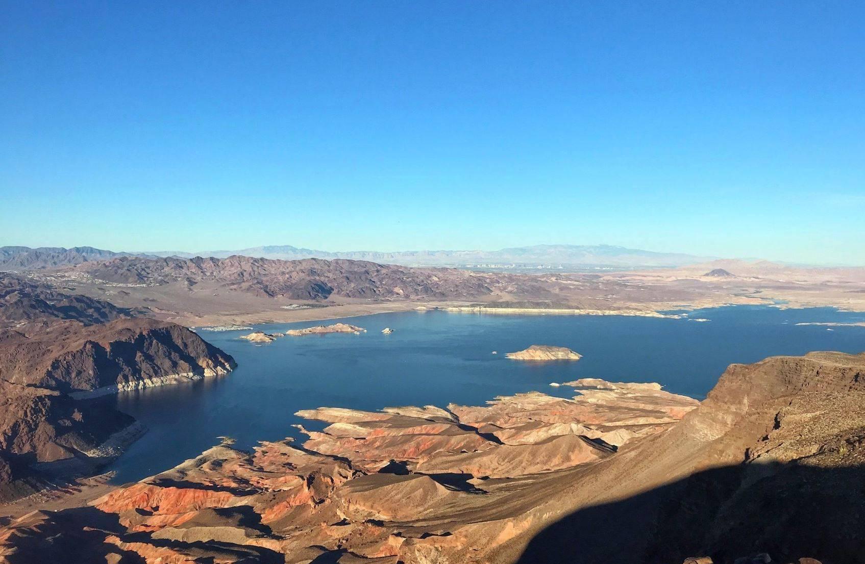 Vast blue lake surrounded by arid, rocky mountains under a clear sky.