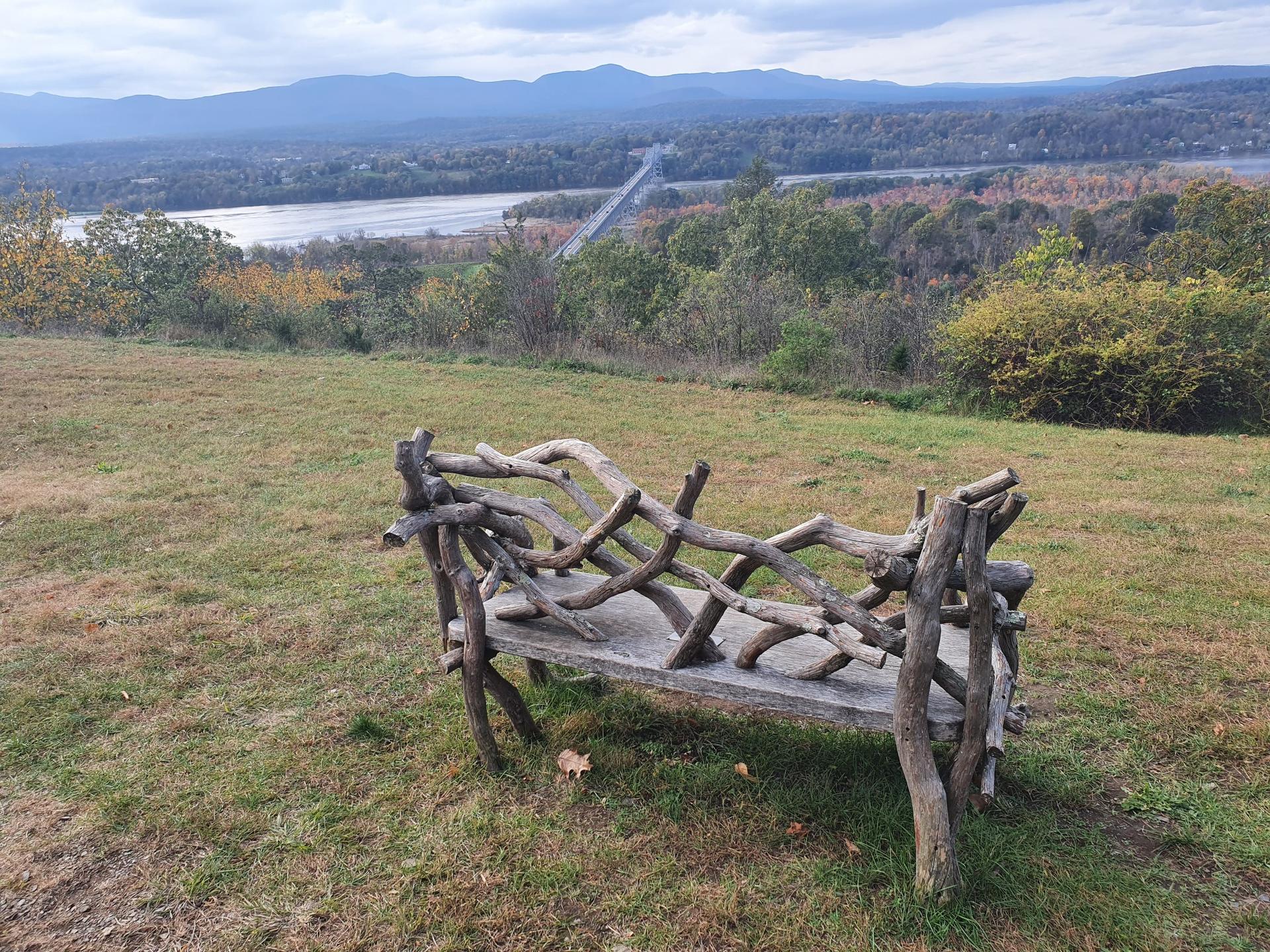 Rustic wooden bench on a hill overlooking a river and mountains.