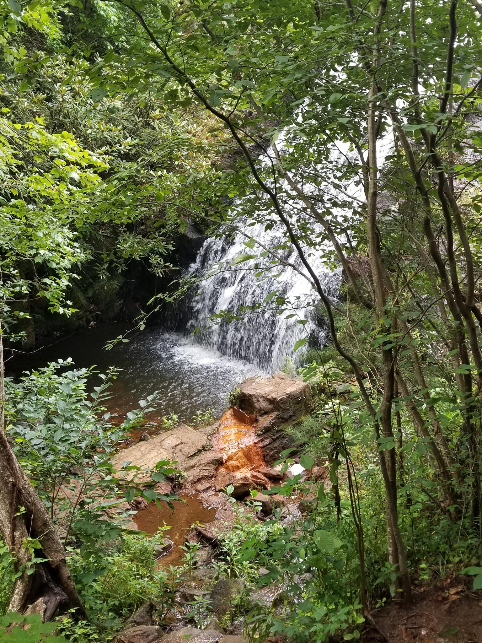 A small waterfall tumbles over reddish rocks into a clear pool.