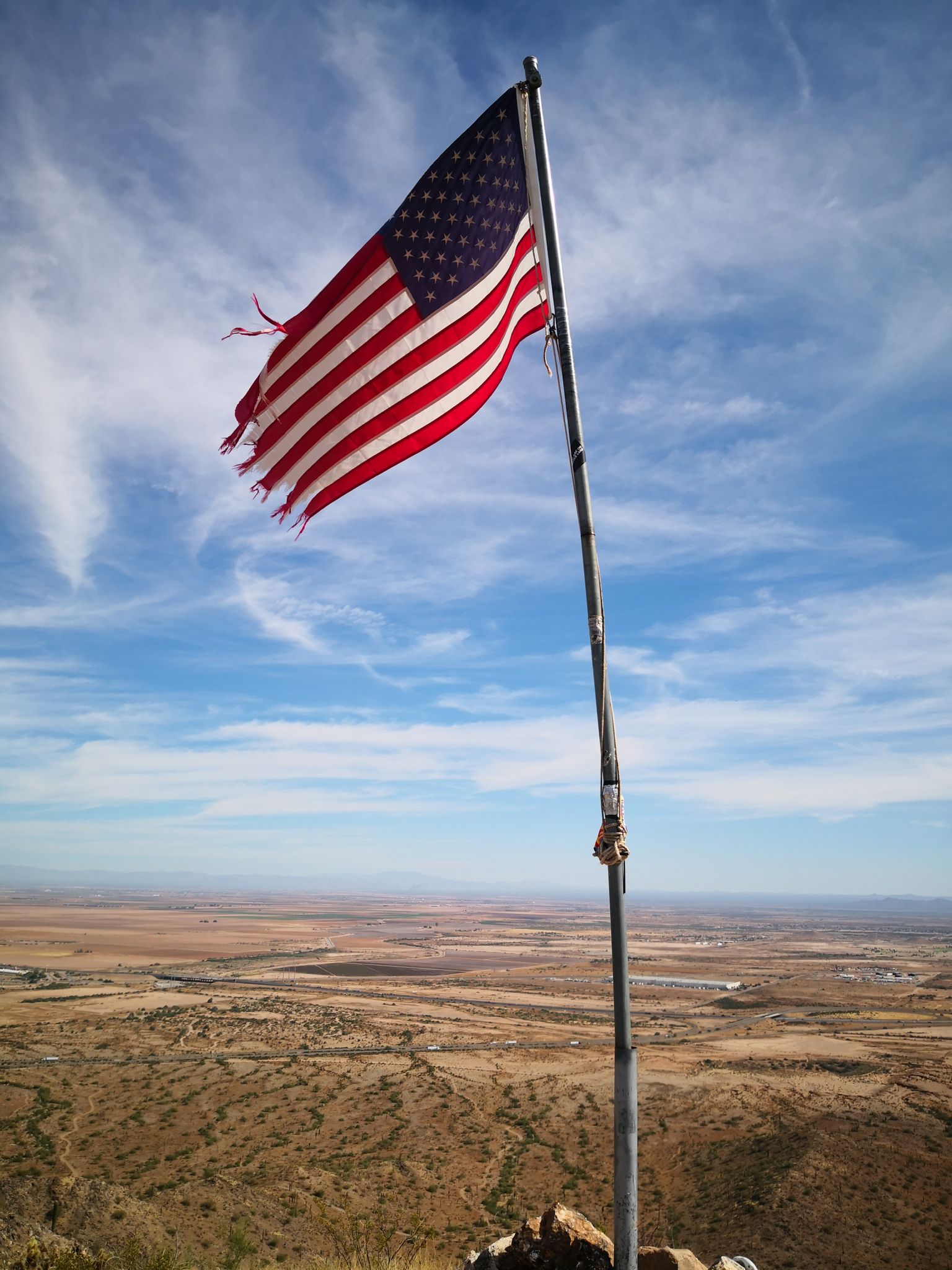 Tattered American flag flying high above a vast desert landscape. - Bolt Trail