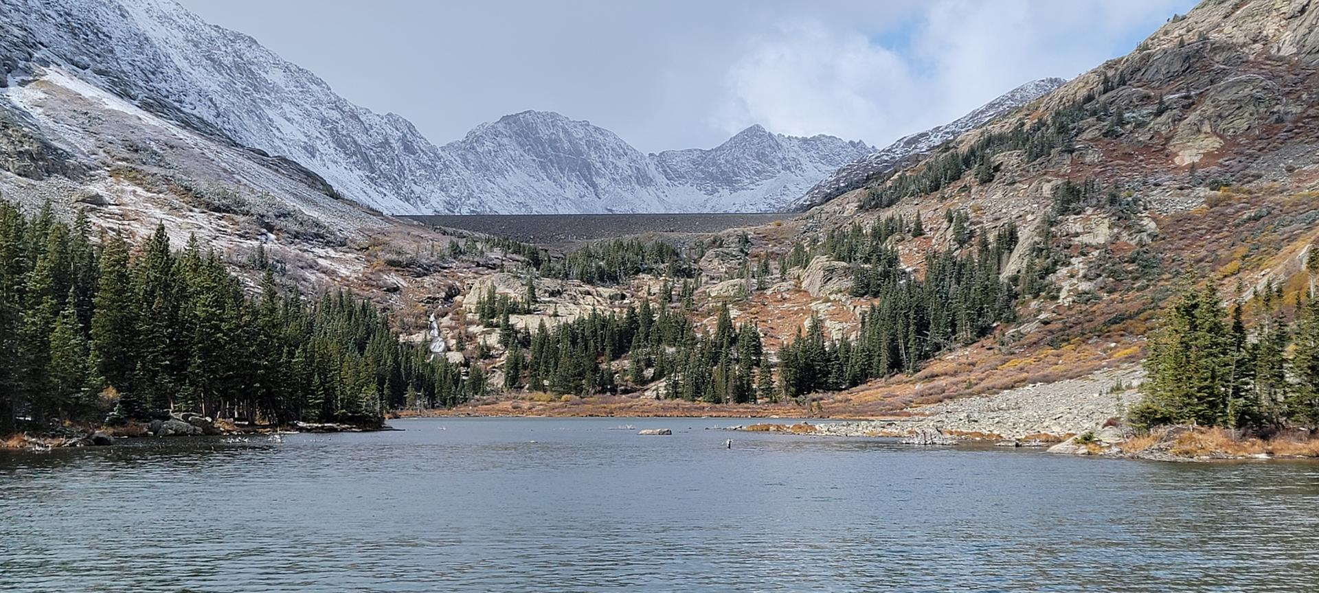 A serene mountain lake surrounded by snow-dusted peaks and dense evergreen forests.