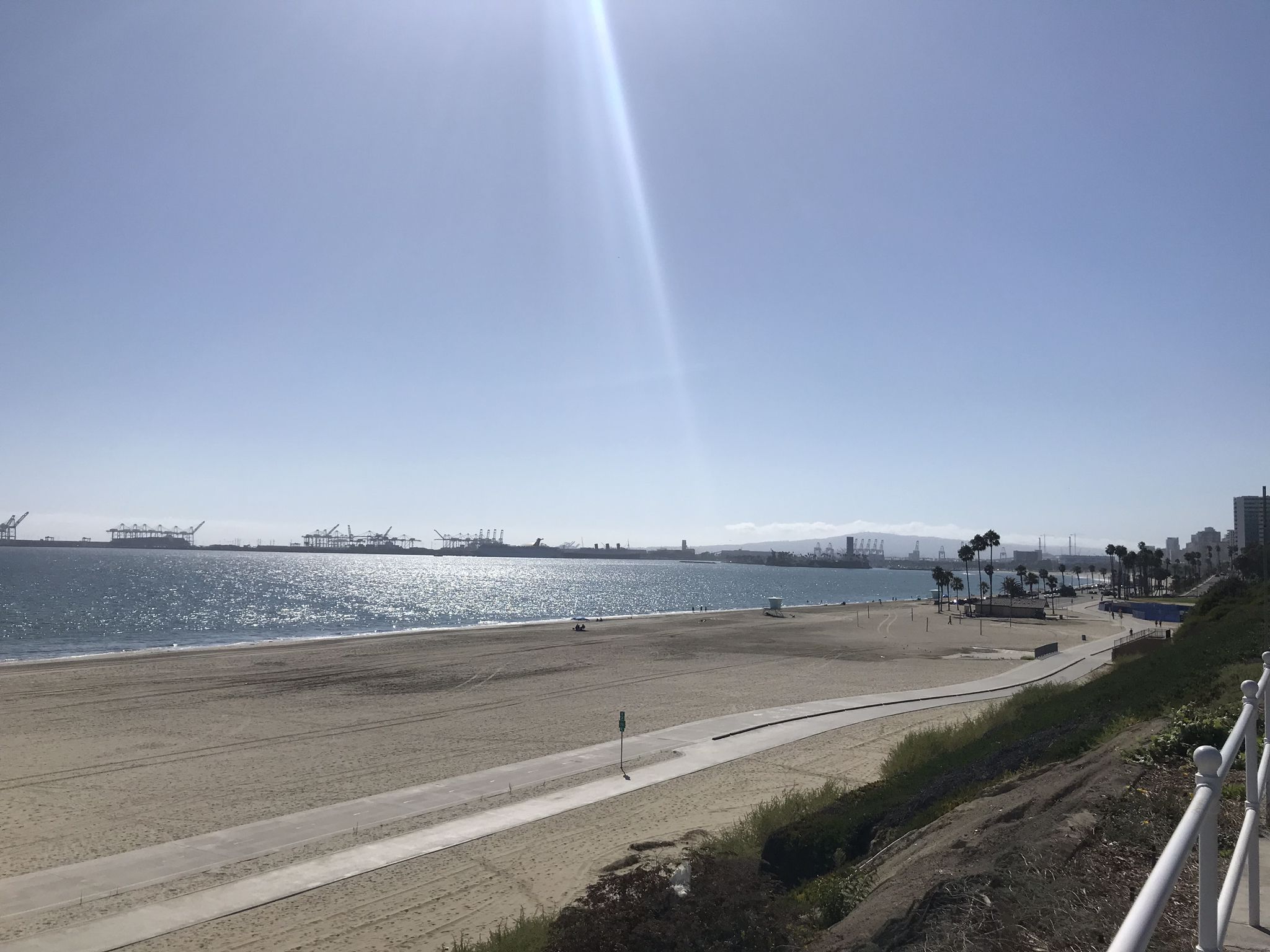 Sunny beach with calm ocean, distant harbor, and bright sky. - Beautiful Beach Bike Path – Long Beach City Beach loop from Hawaiian Gardens