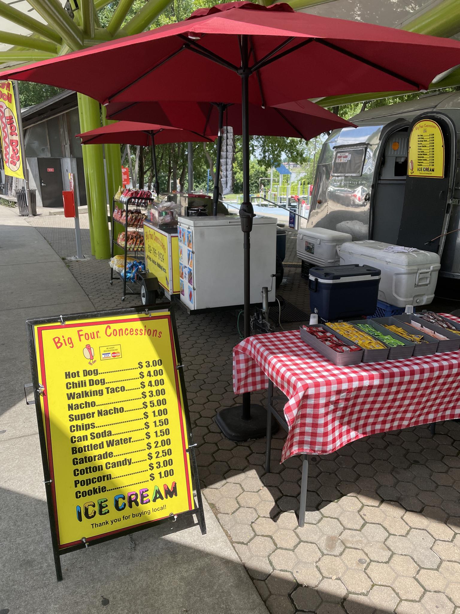 A concession stand with red umbrellas, a menu, and food items.