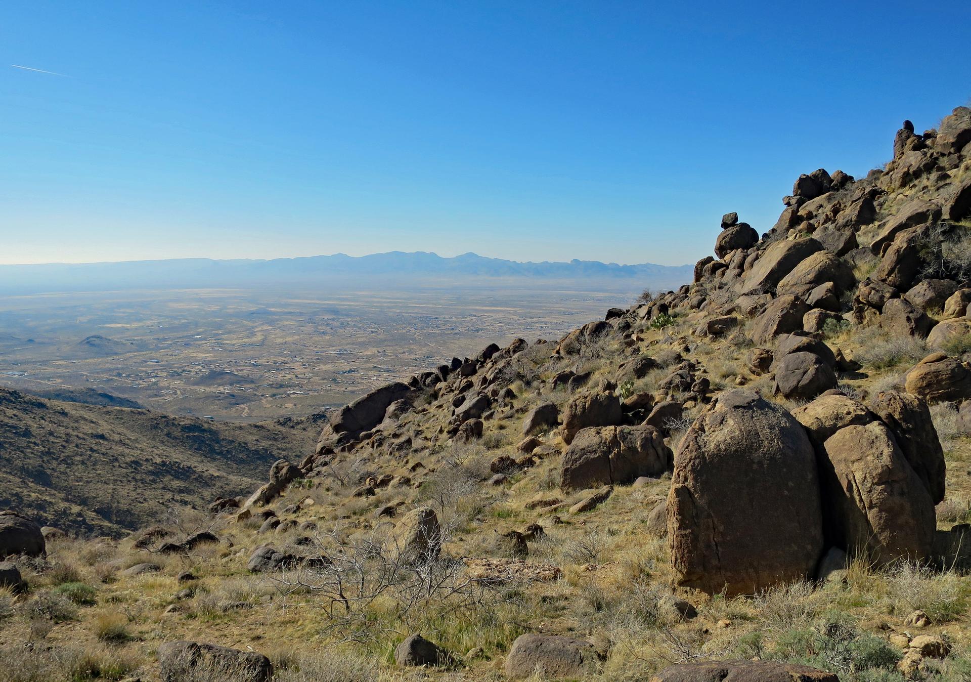 Sunny desert landscape with a rocky hillside overlooking a vast valley.