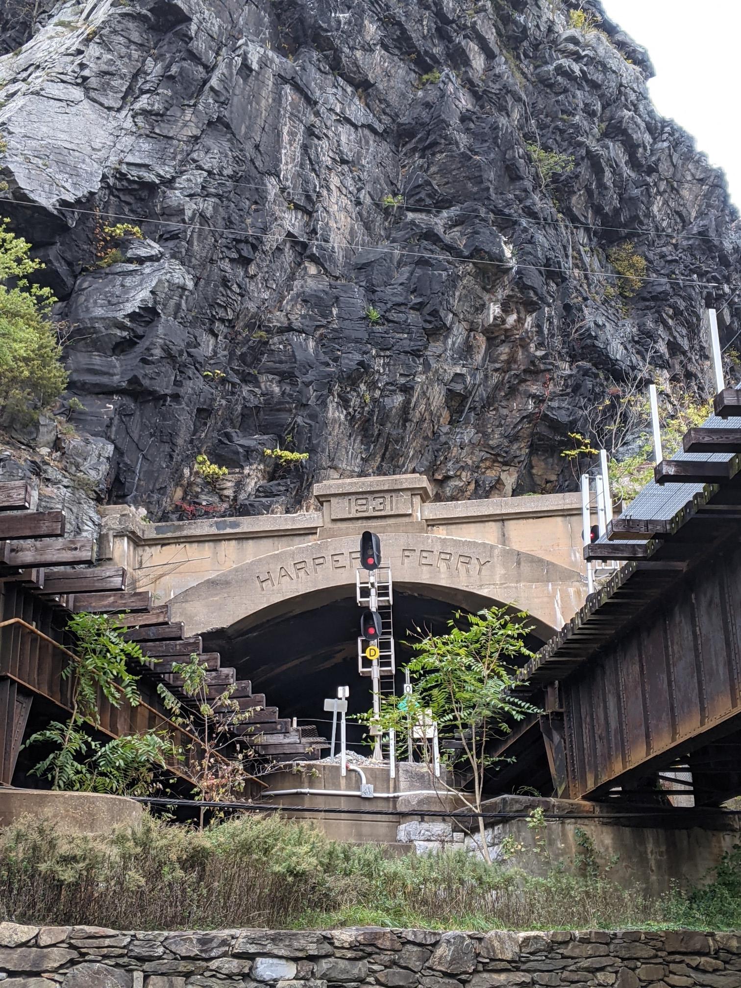 Stone tunnel entrance under a rocky cliff with adjacent metal bridge structures.
