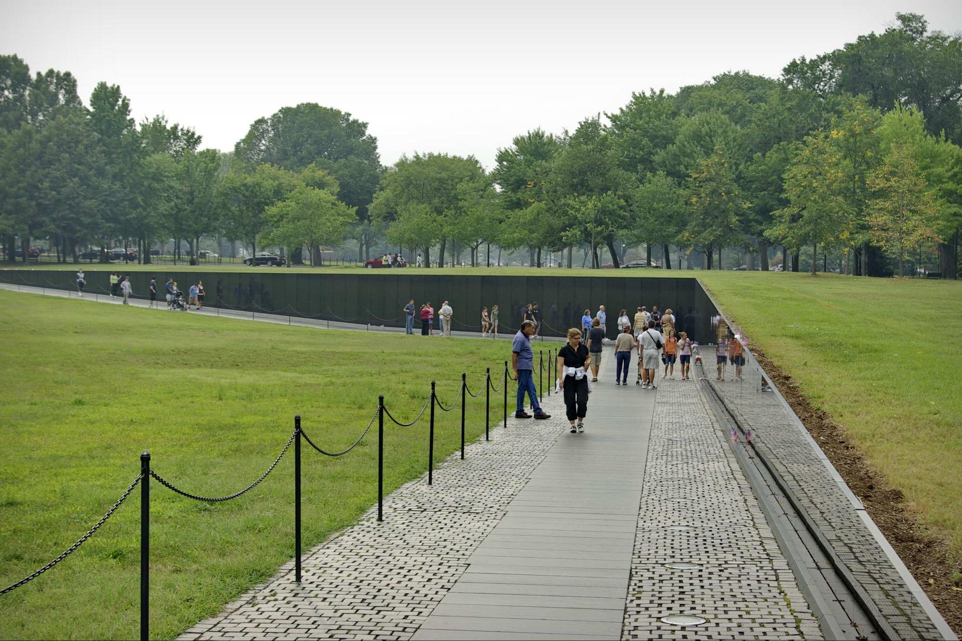 People walking along a path next to a dark wall and grassy slope.