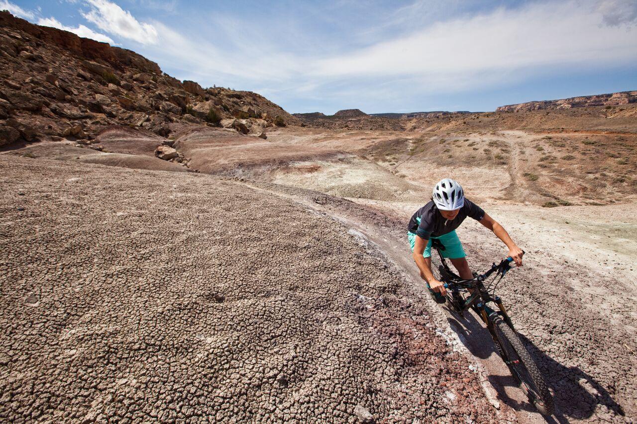 Mountain biker descends a dry, cracked, rocky landscape on a sunny day.