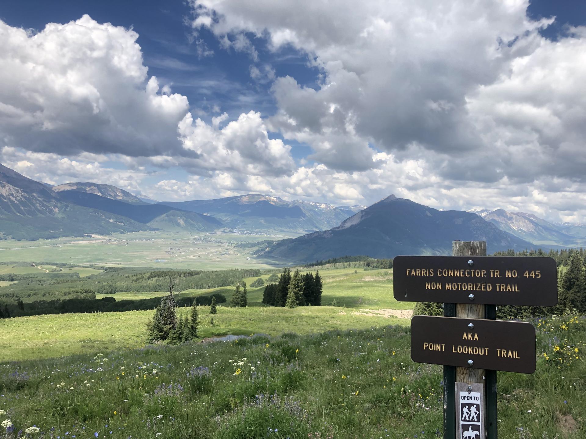 Mountain vista with green fields and a trail sign under a cloudy sky.