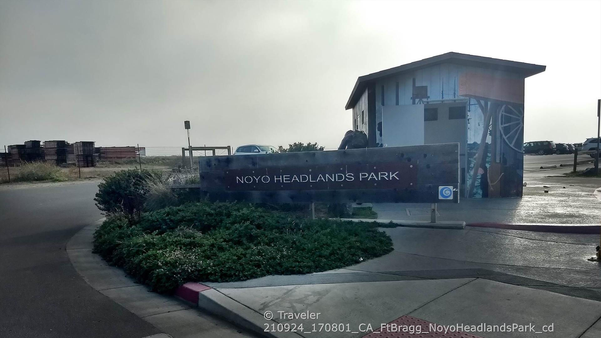 Overcast view of a park entrance sign and a small building.