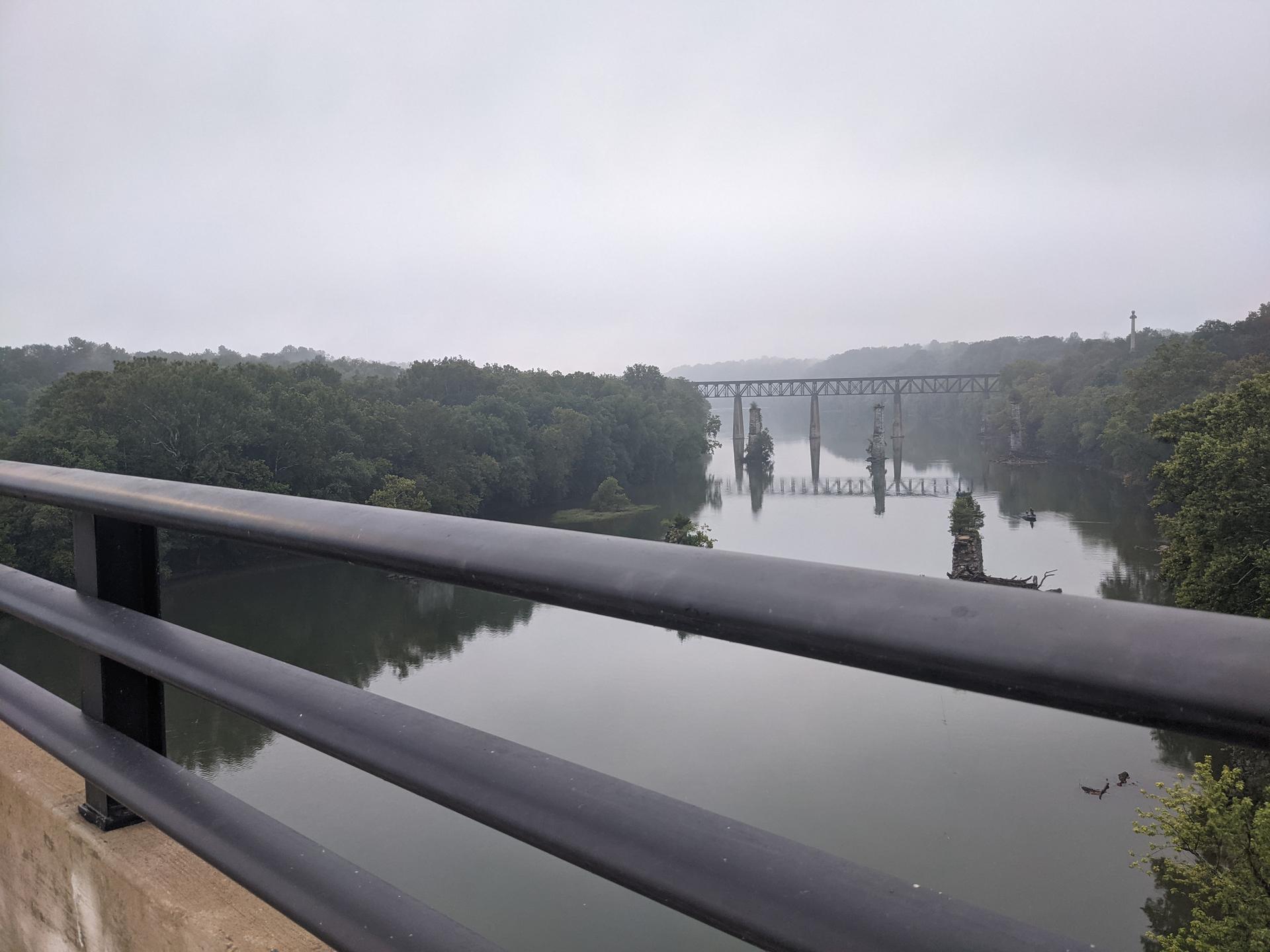 Overcast river view with bridge piers and distant bridge, seen from behind a railing.