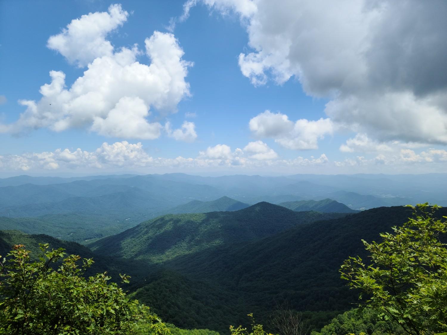 Green mountain valleys under a bright blue sky with fluffy white clouds.