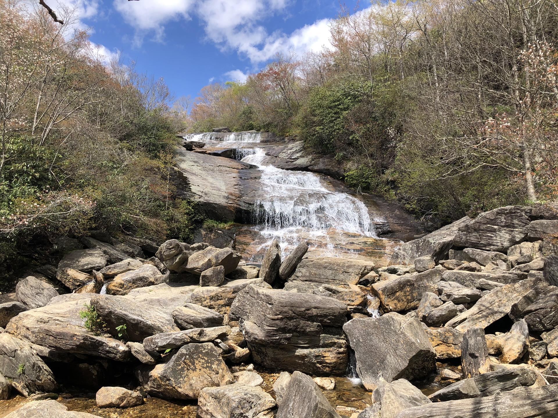 Wide waterfall cascading over a large rock face, surrounded by trees.