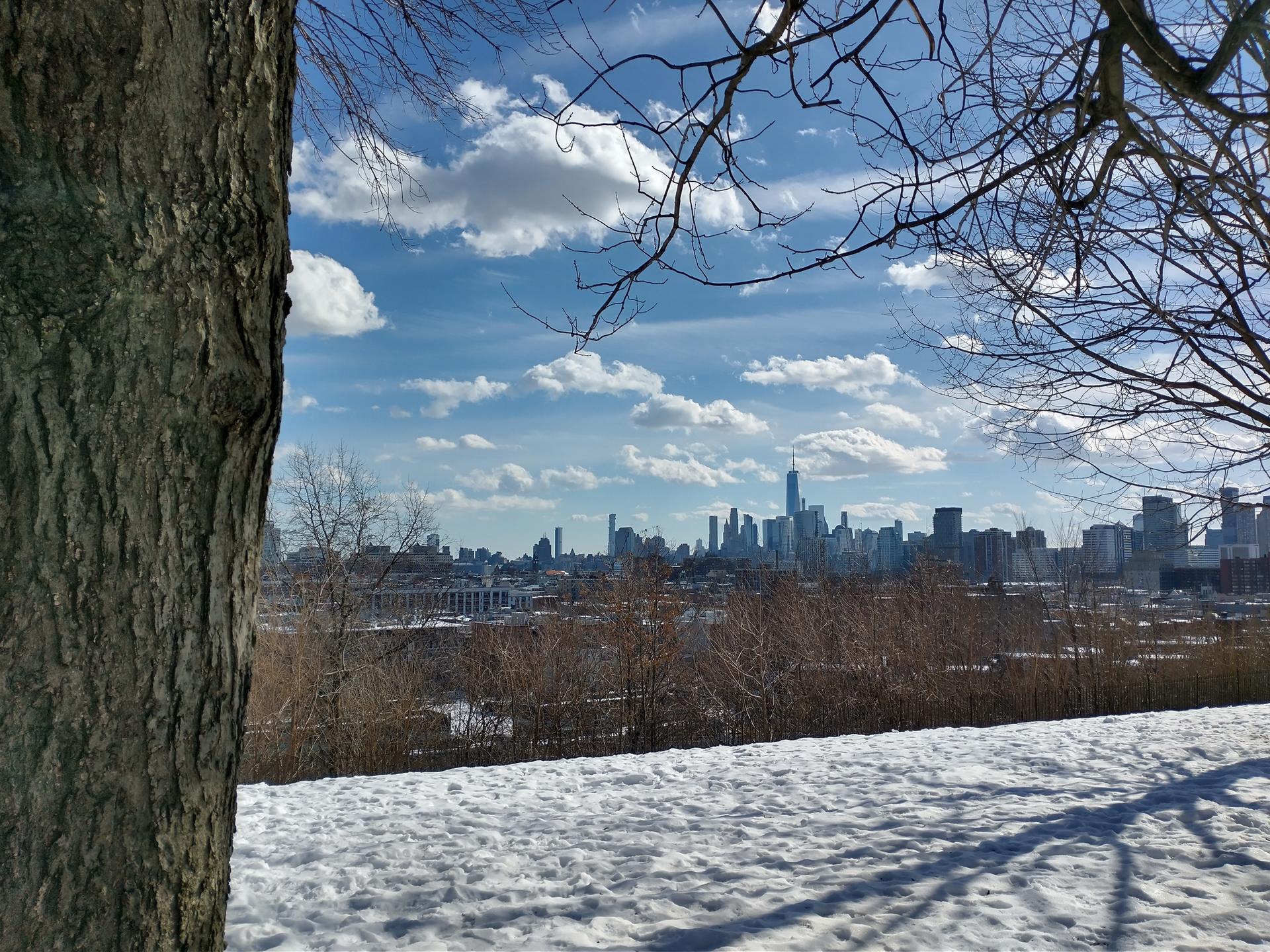 Sunny winter view of a distant city skyline over a snowy hill.