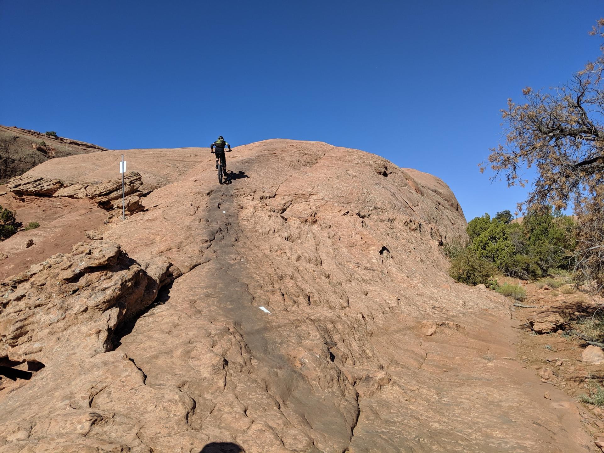 Mountain biker ascending a steep, reddish rock face under a clear sky.