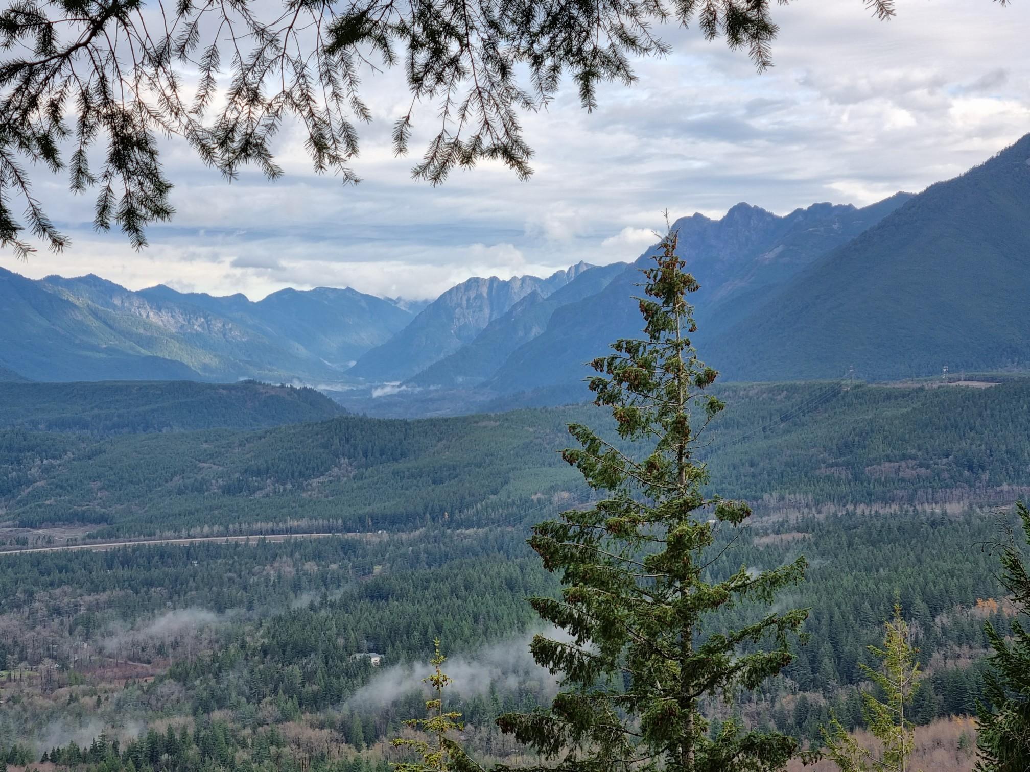 Expansive mountain valley with dense evergreen forests under a cloudy sky.