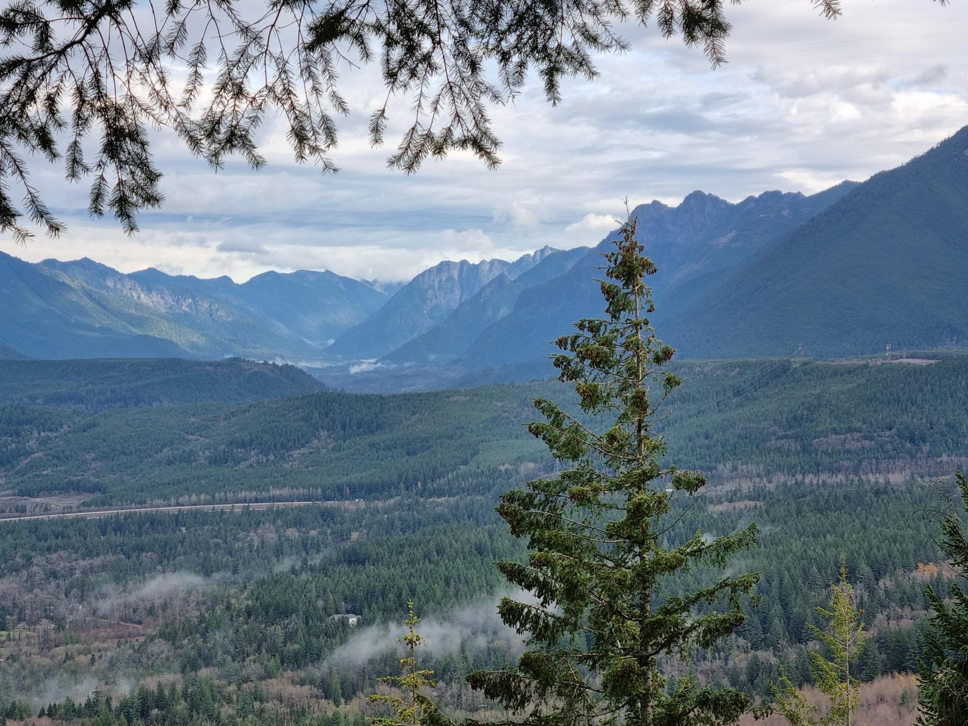 Expansive mountain valley with dense evergreen forests under a cloudy sky.