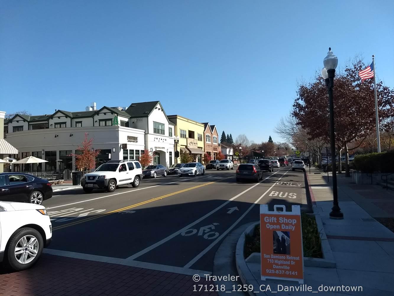 Bright urban street with cars, buildings, and a bus lane on a clear day.