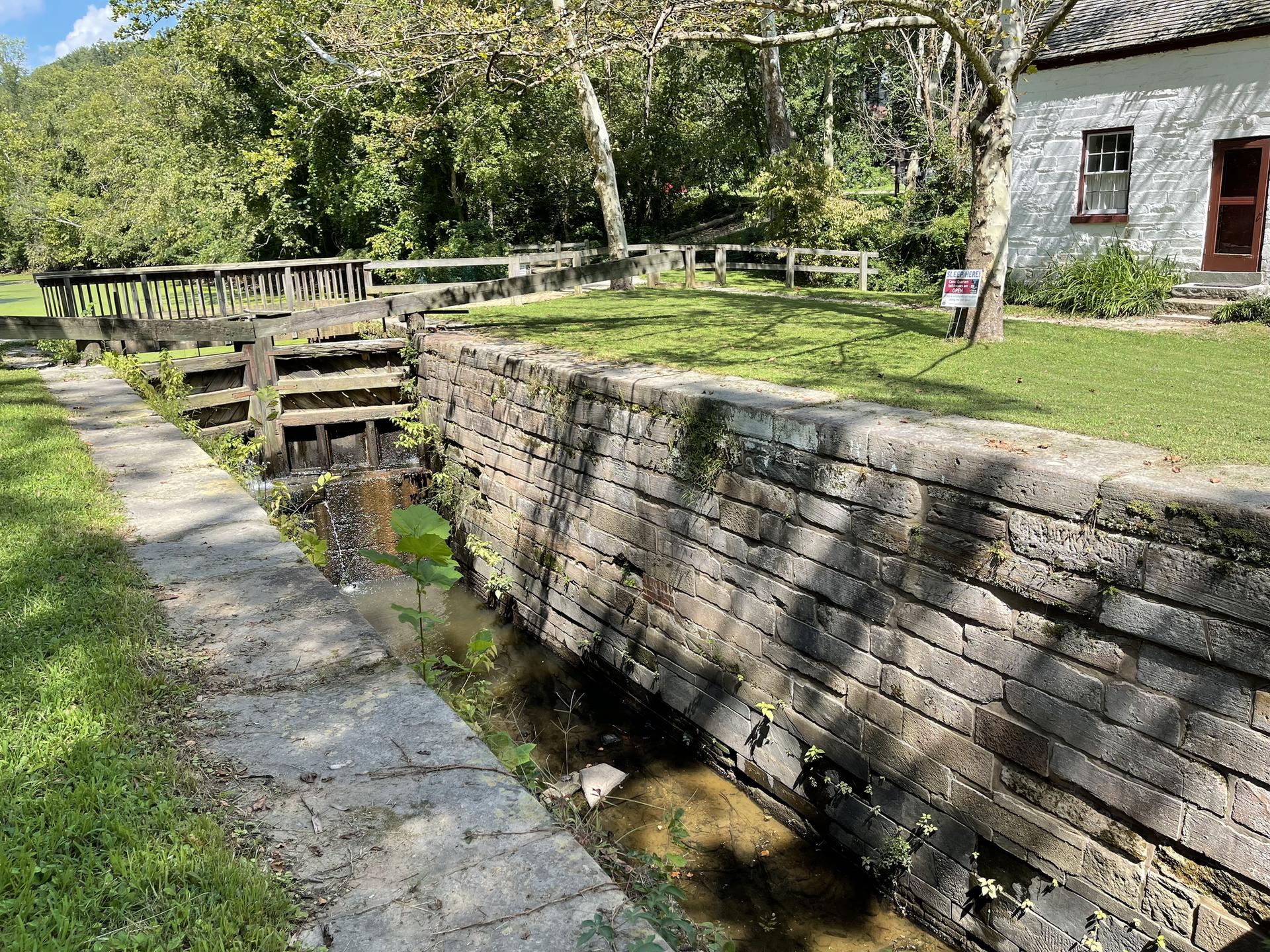 A historic stone canal lock next to a white building on a sunny day.