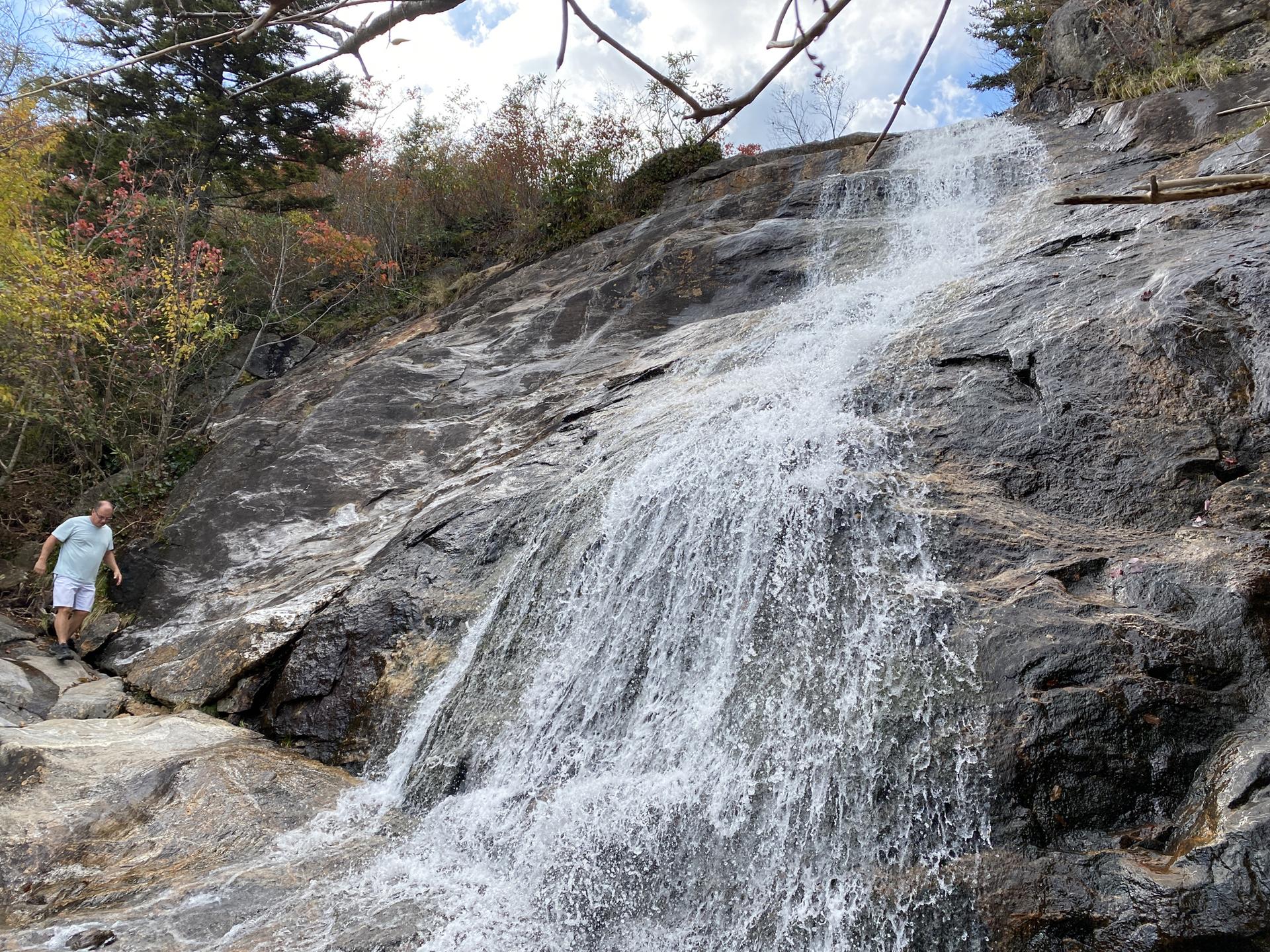 Man standing beside a powerful waterfall cascading down a rocky cliff.