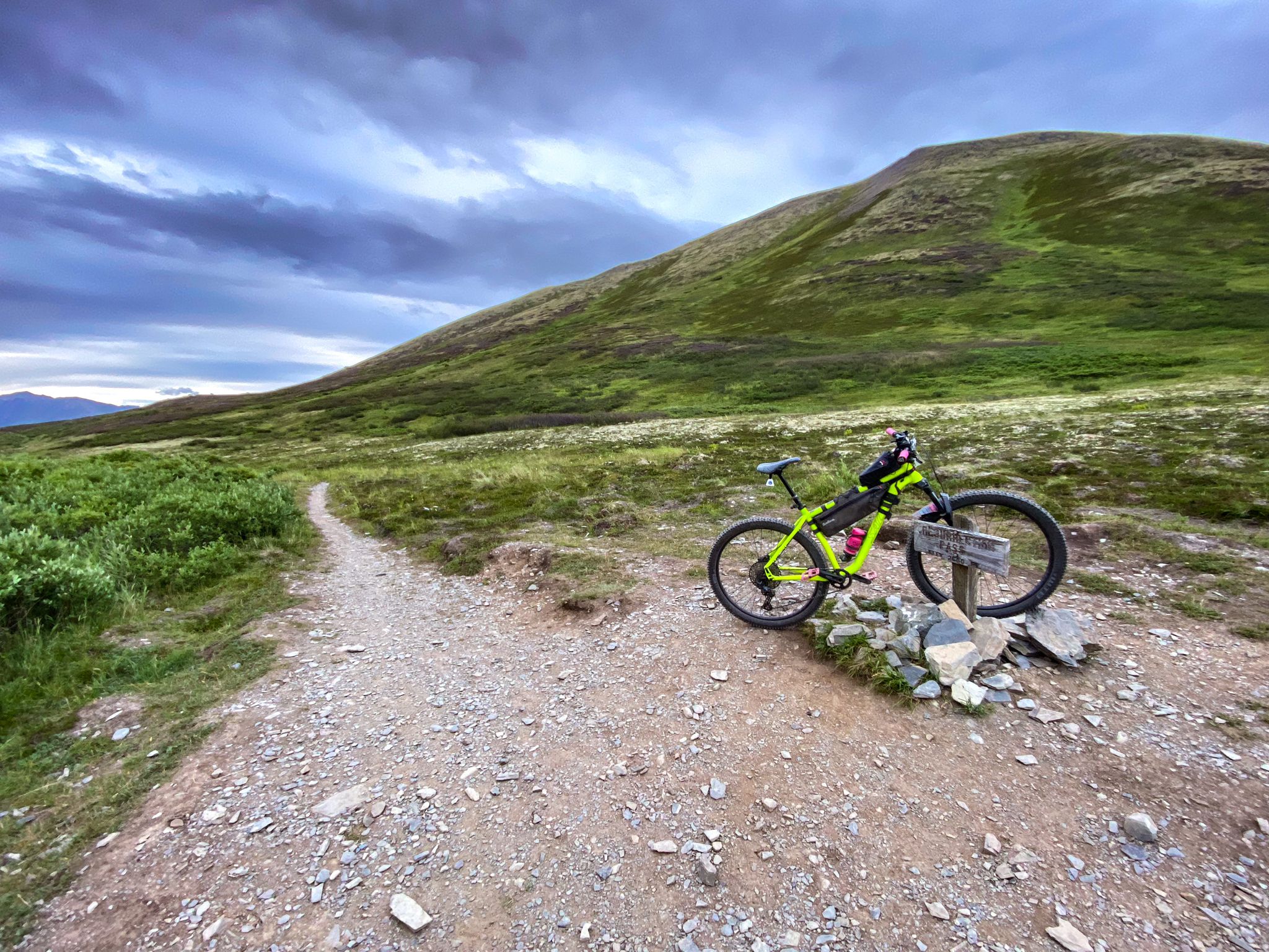 A bright green mountain bike rests on a rocky trail under cloudy skies. - Resurrection Pass Trail