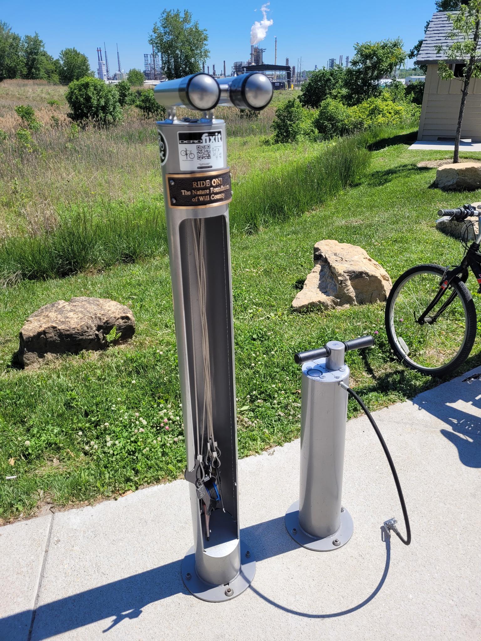 A bicycle repair station and pump on a concrete path on a sunny day.