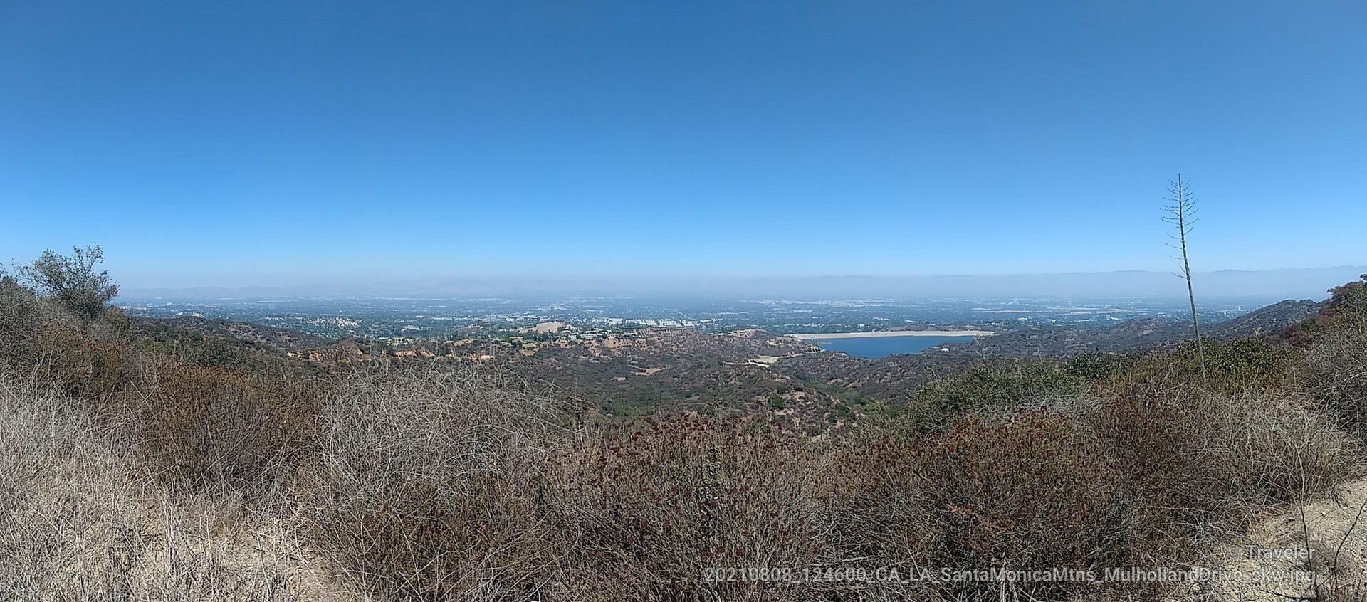Panoramic view of a city and lake from a dry, brushy hillside.