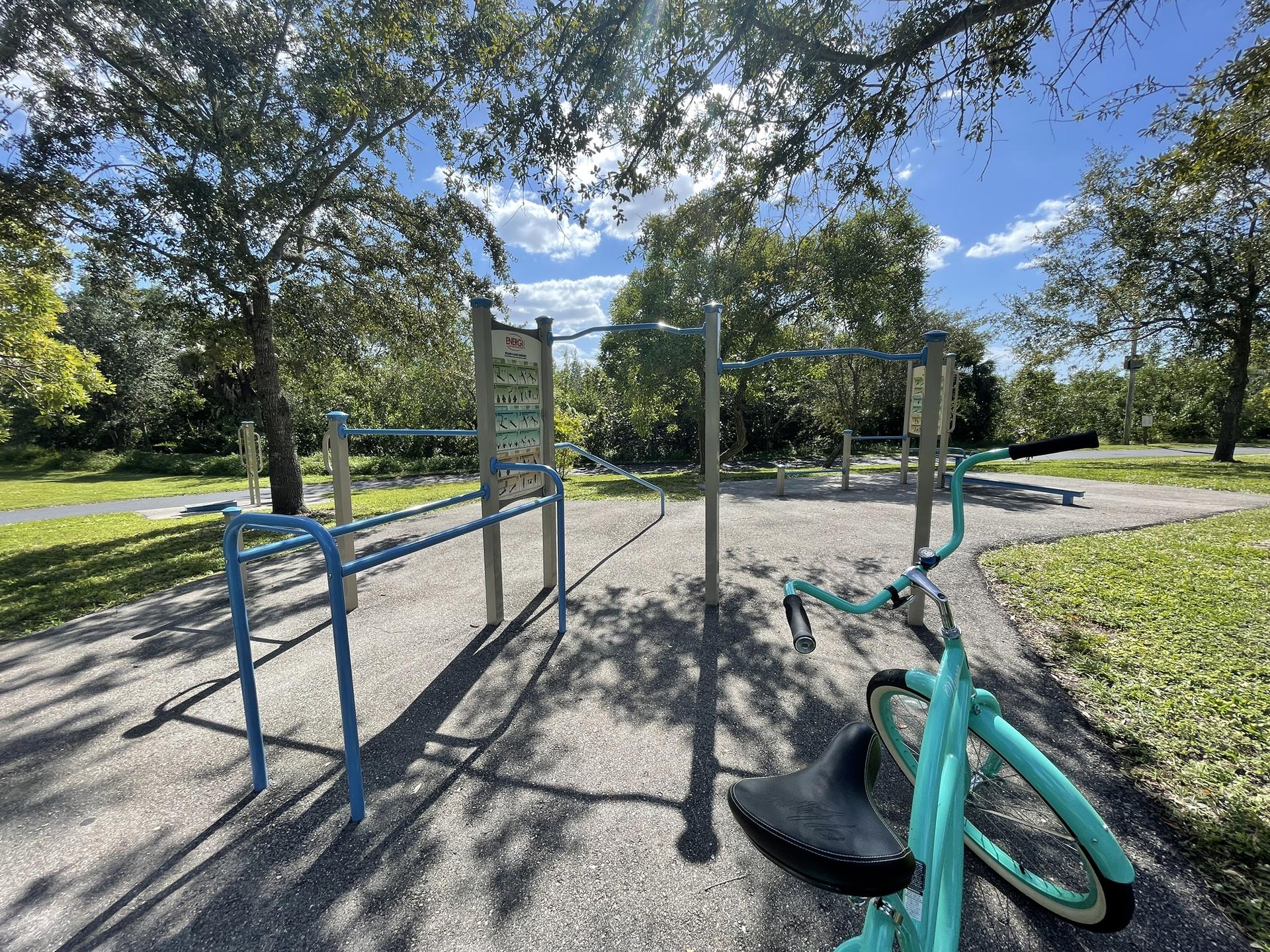 Outdoor exercise equipment and a bicycle on a paved path in a sunny park.