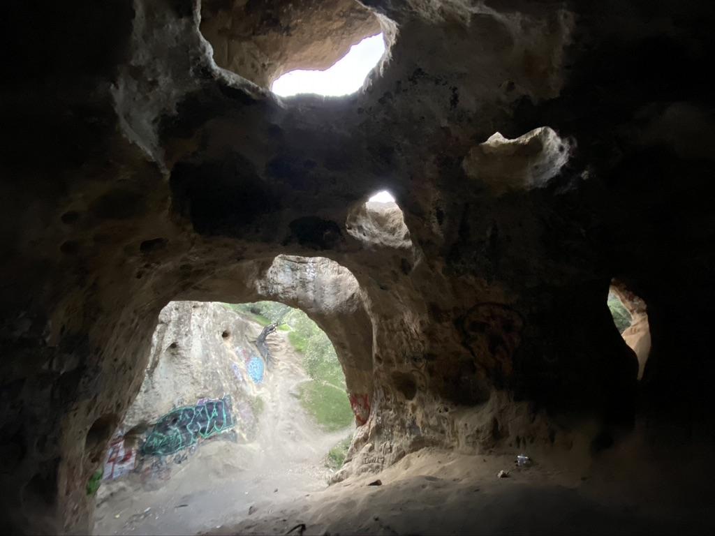 Inside a dark cave with multiple openings letting in bright natural light.