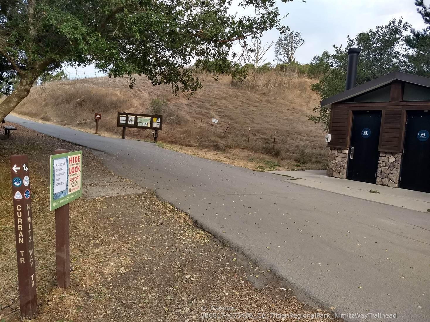Paved path leading to a brown building with restrooms and signs.