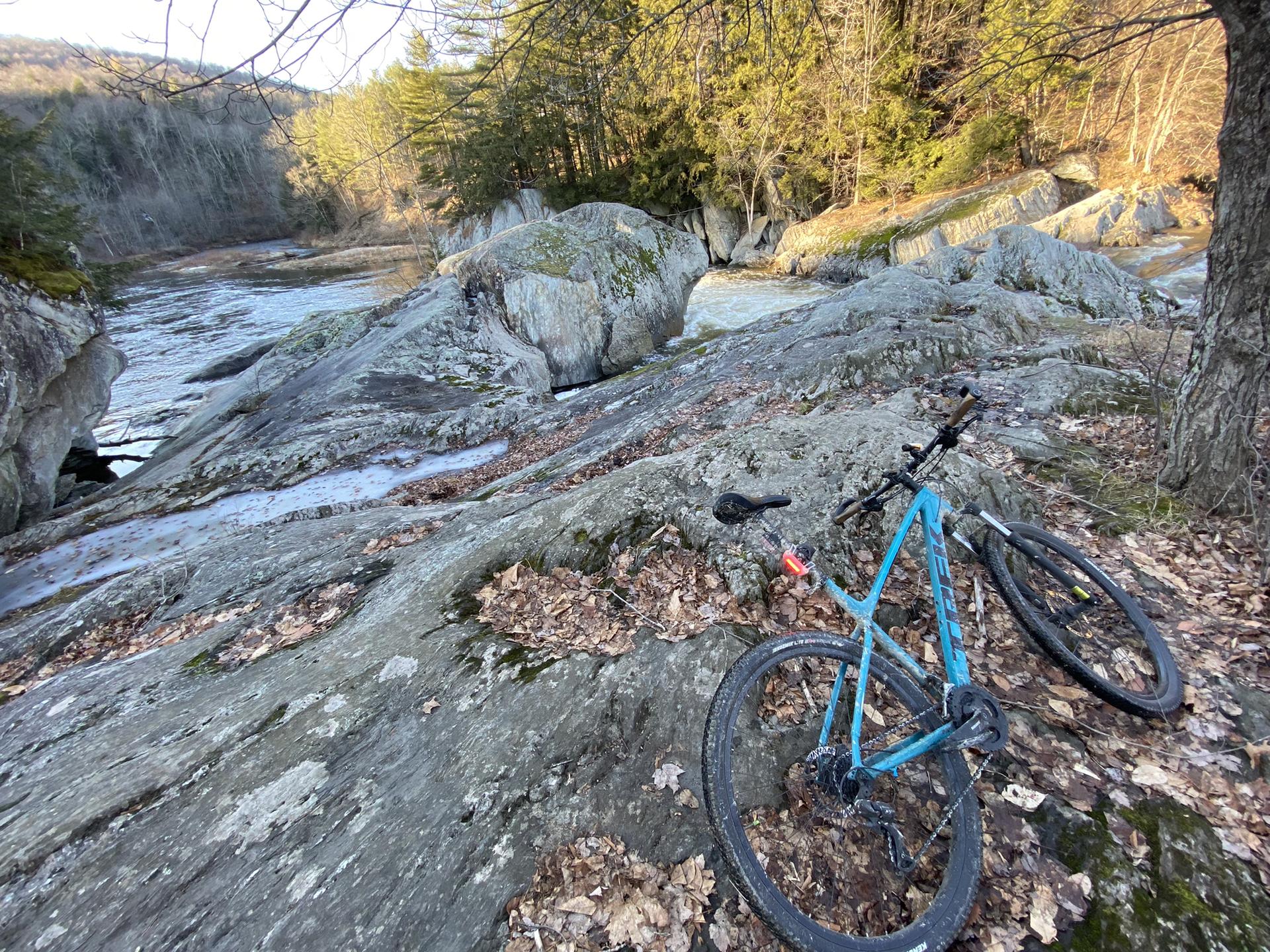 A blue mountain bike rests on large rocks beside a flowing river.