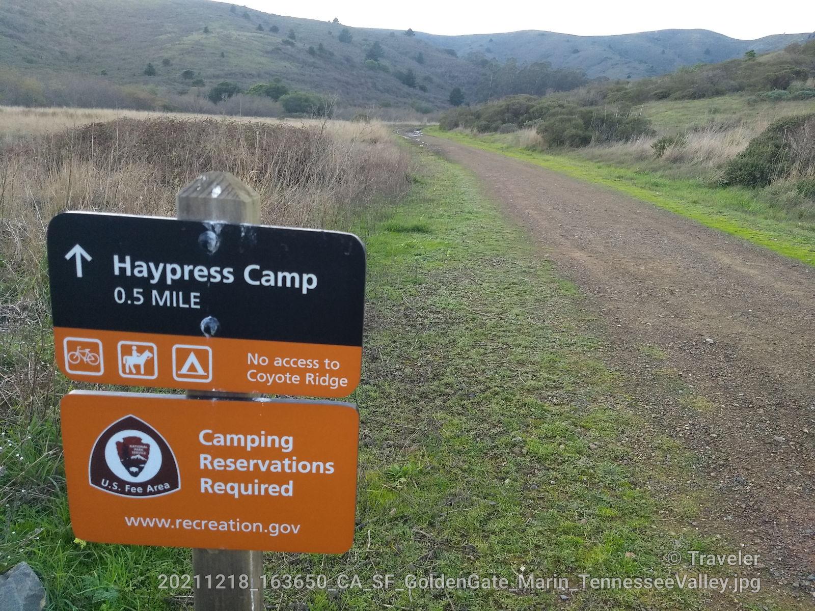 A trail sign points to a dirt path winding through grassy hills.